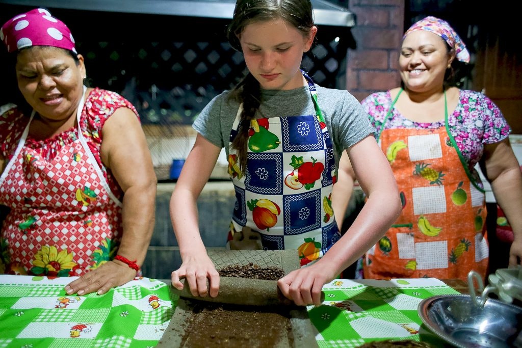 A student is baking with the help of two ladies.