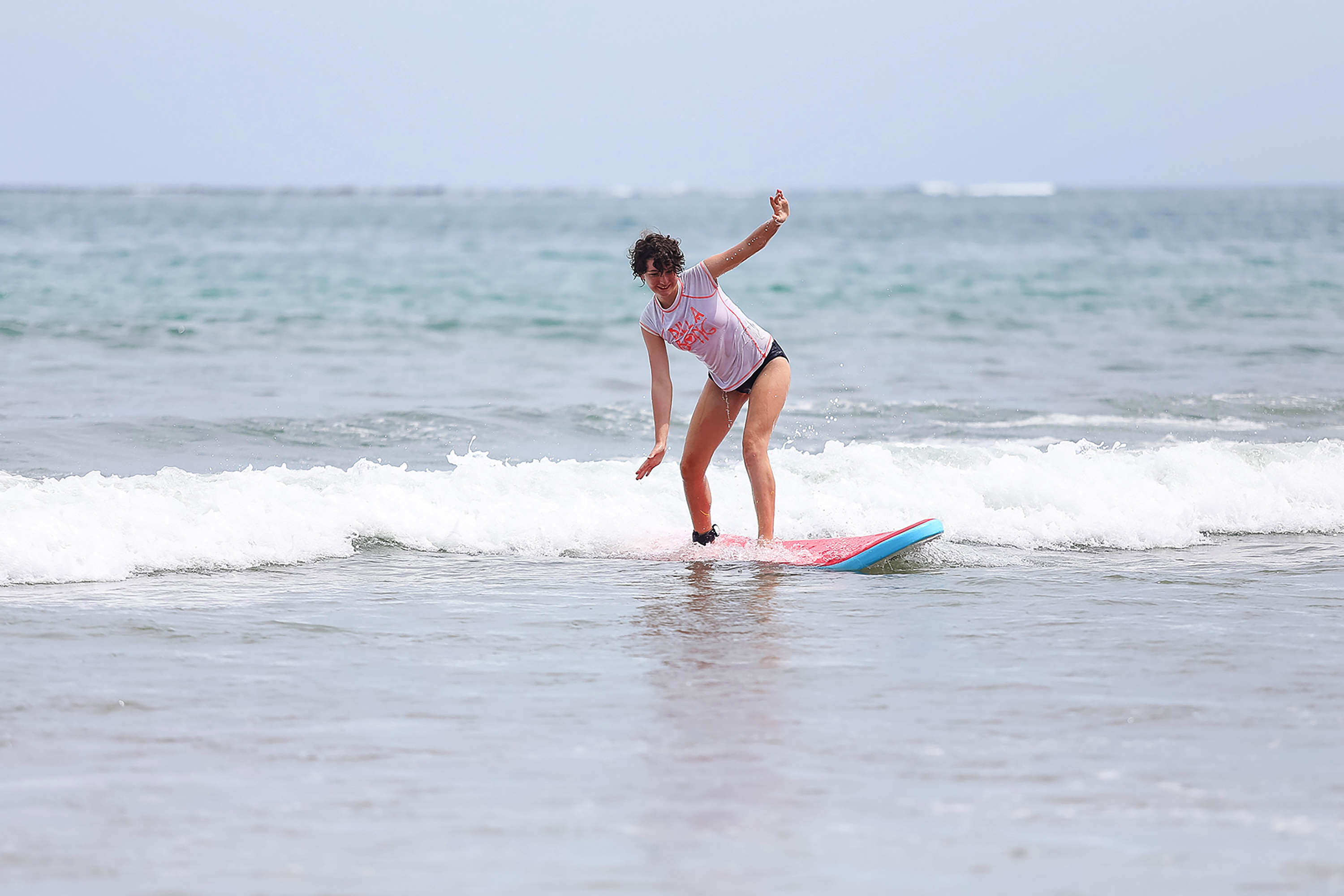 A student balances on a surfboard while catching a small wave