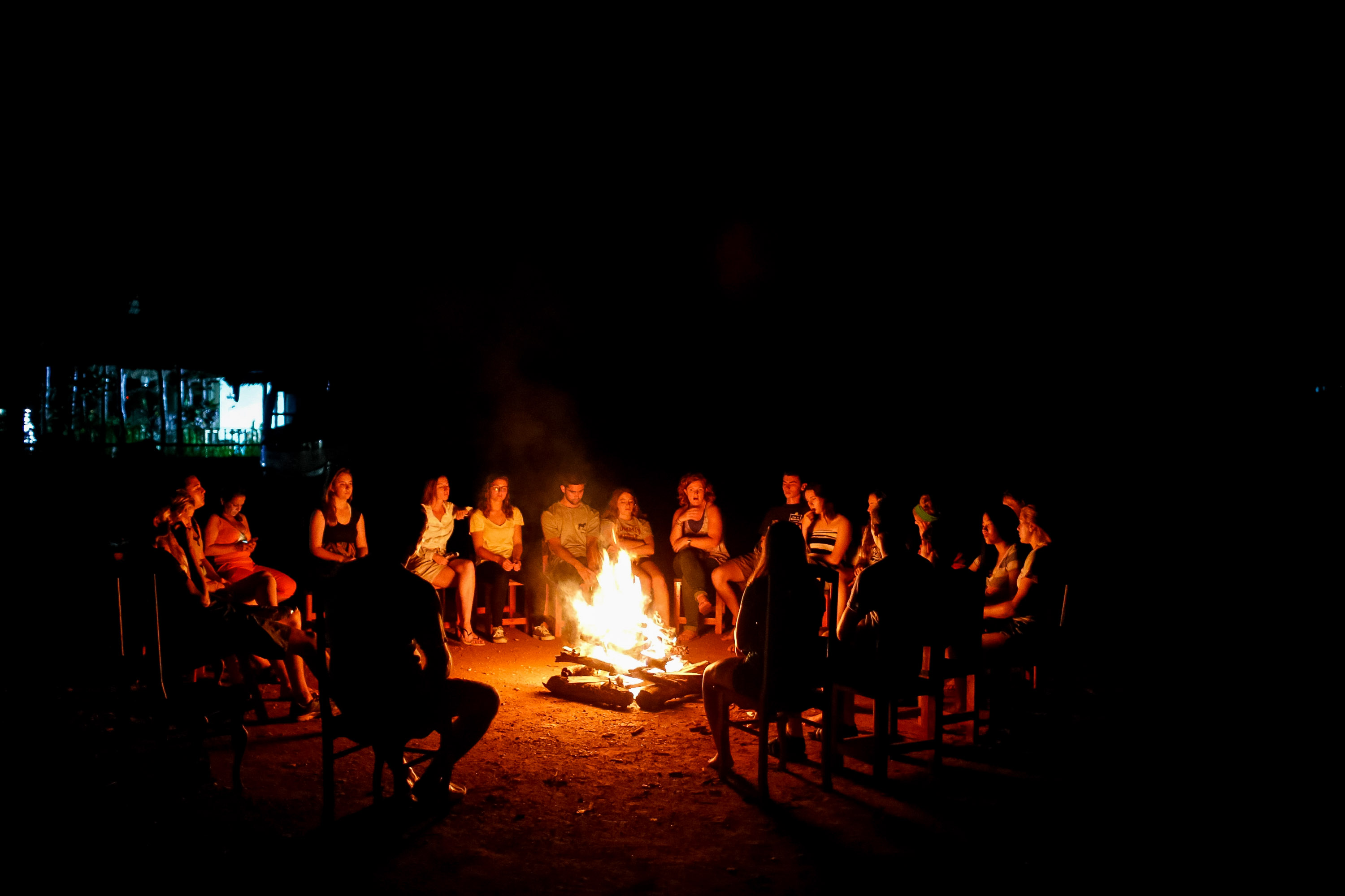 Students sit in a circle around a glowing bonfire at night