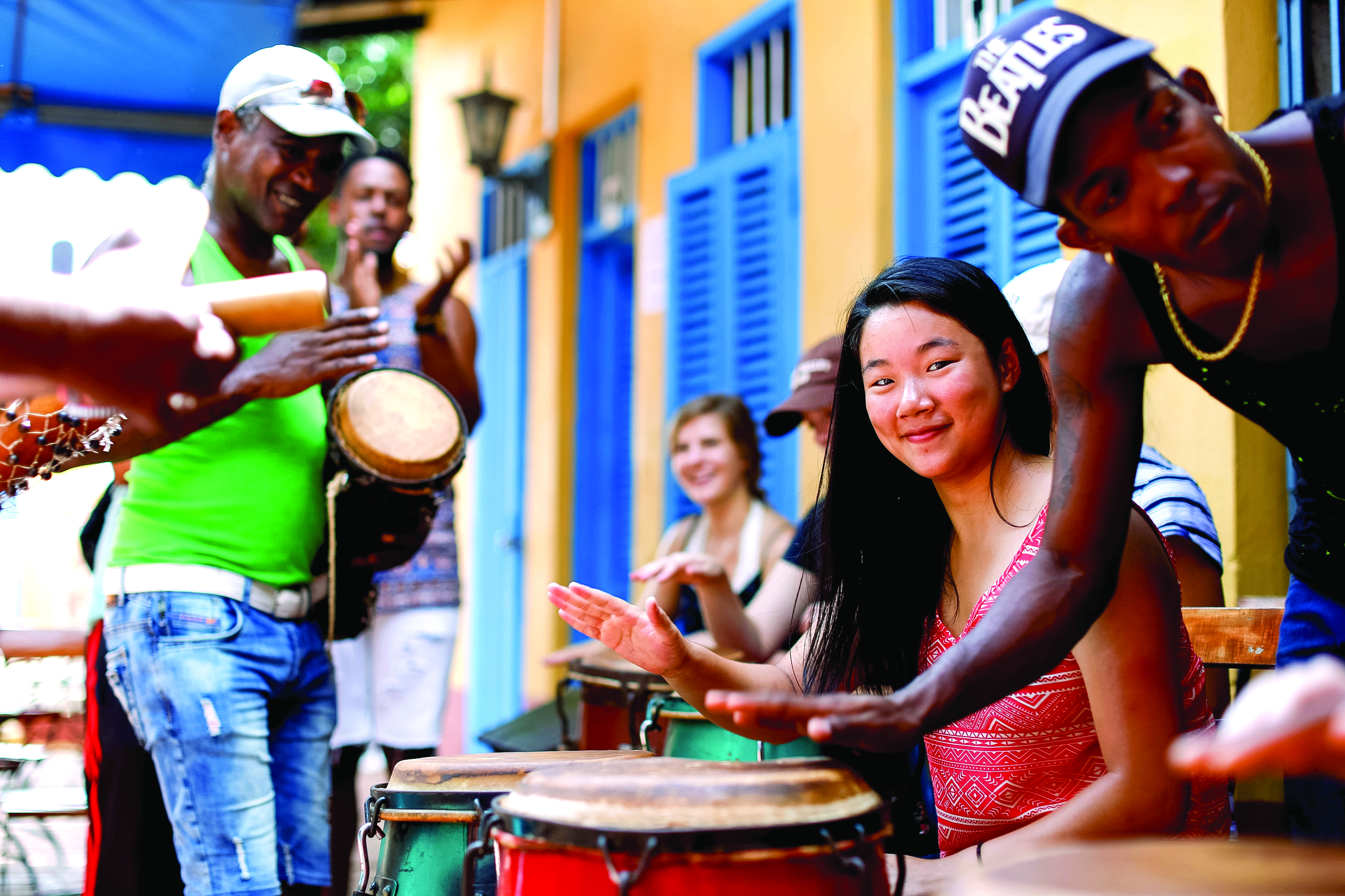 Students play conga drums alongside local musicians on a colorful street