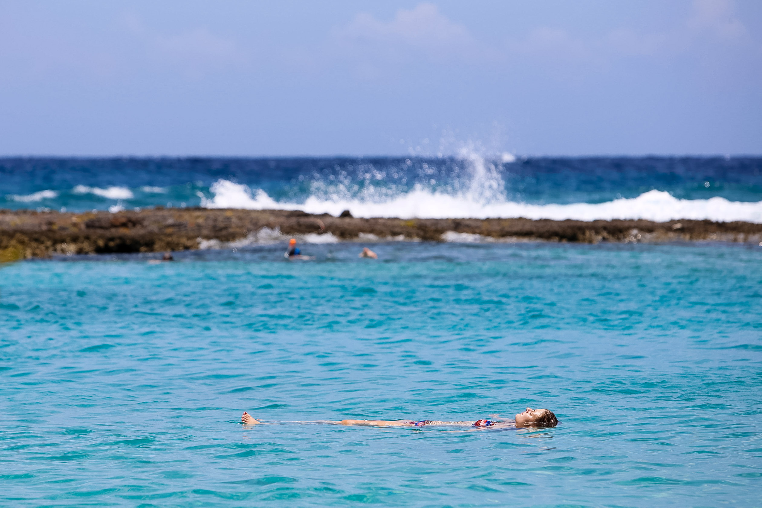 A student floats on their back in calm turquoise water near a reef
