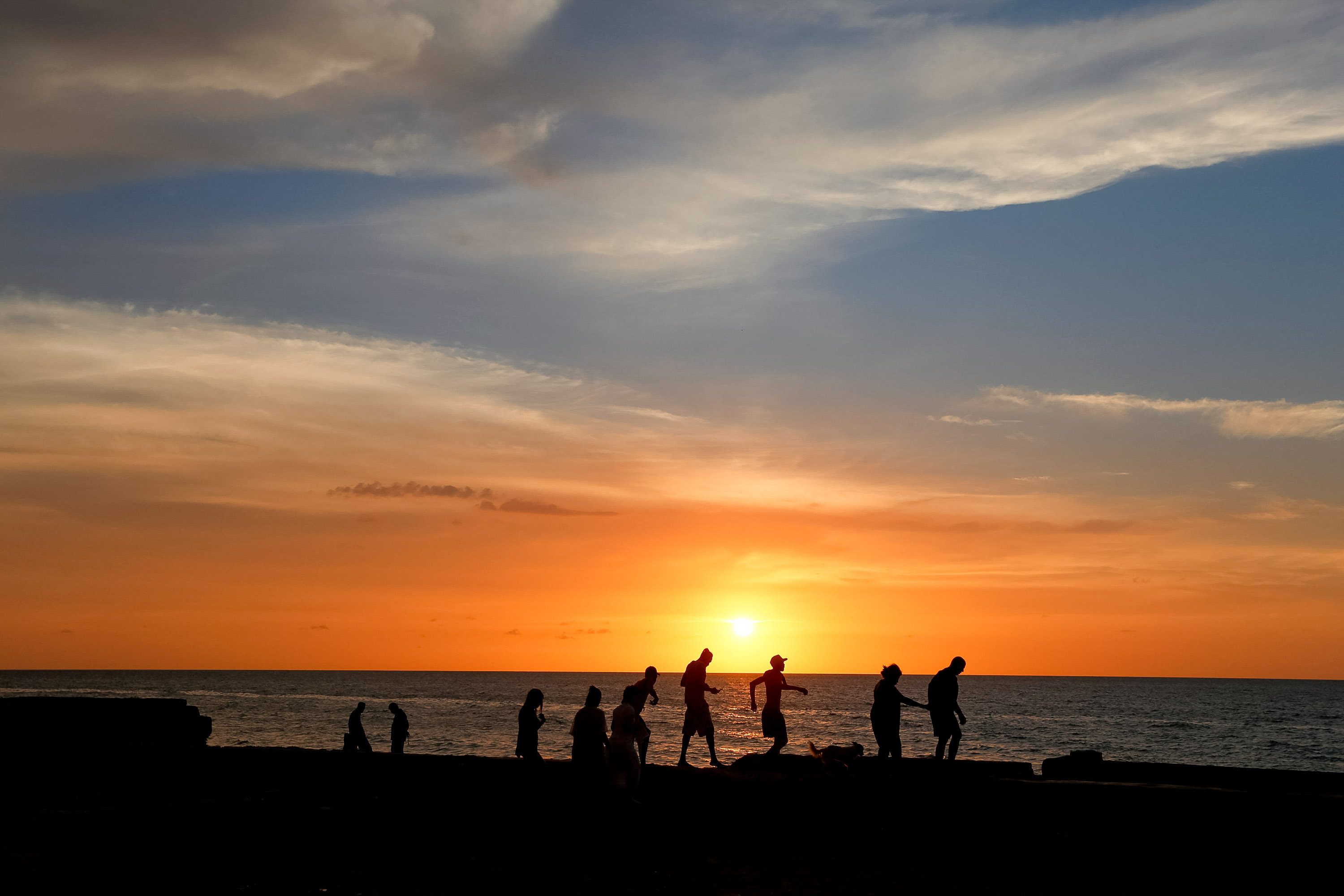 Silhouetted figures walk along a beach as the sun sets over the ocean