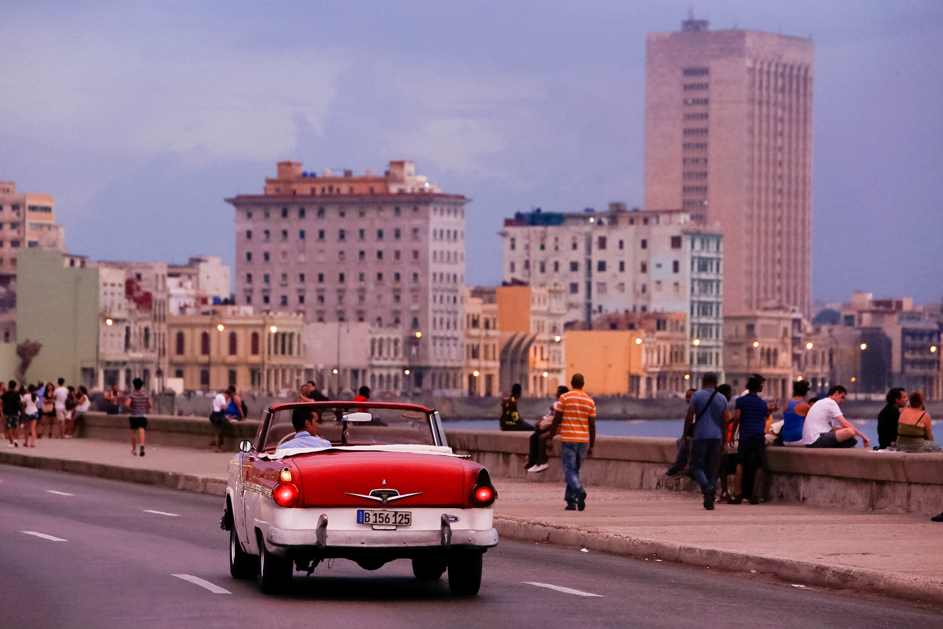 A classic car cruises along Havana's seaside Malecón at dusk with the city skyline behind