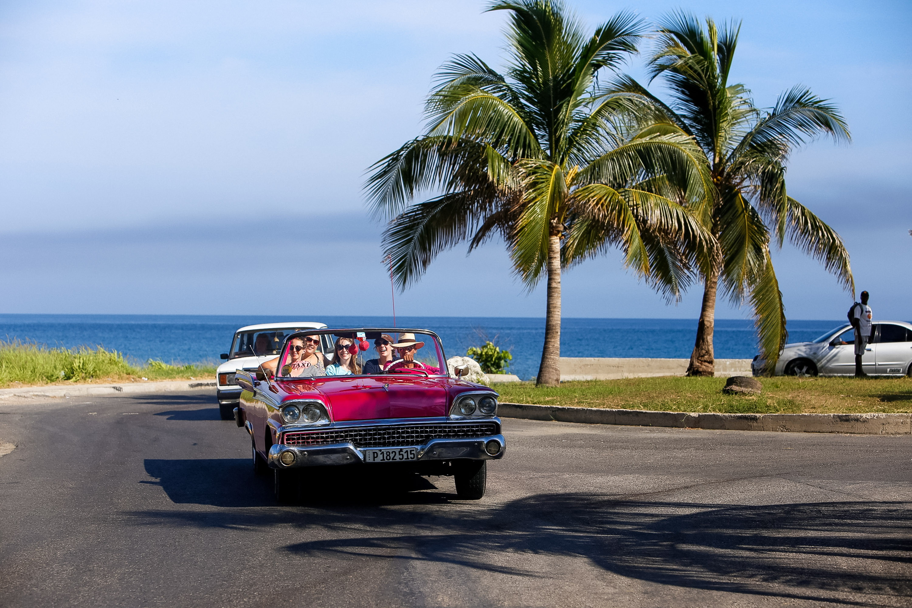 A classic car carries passengers along a palm-lined coastal road in Cuba