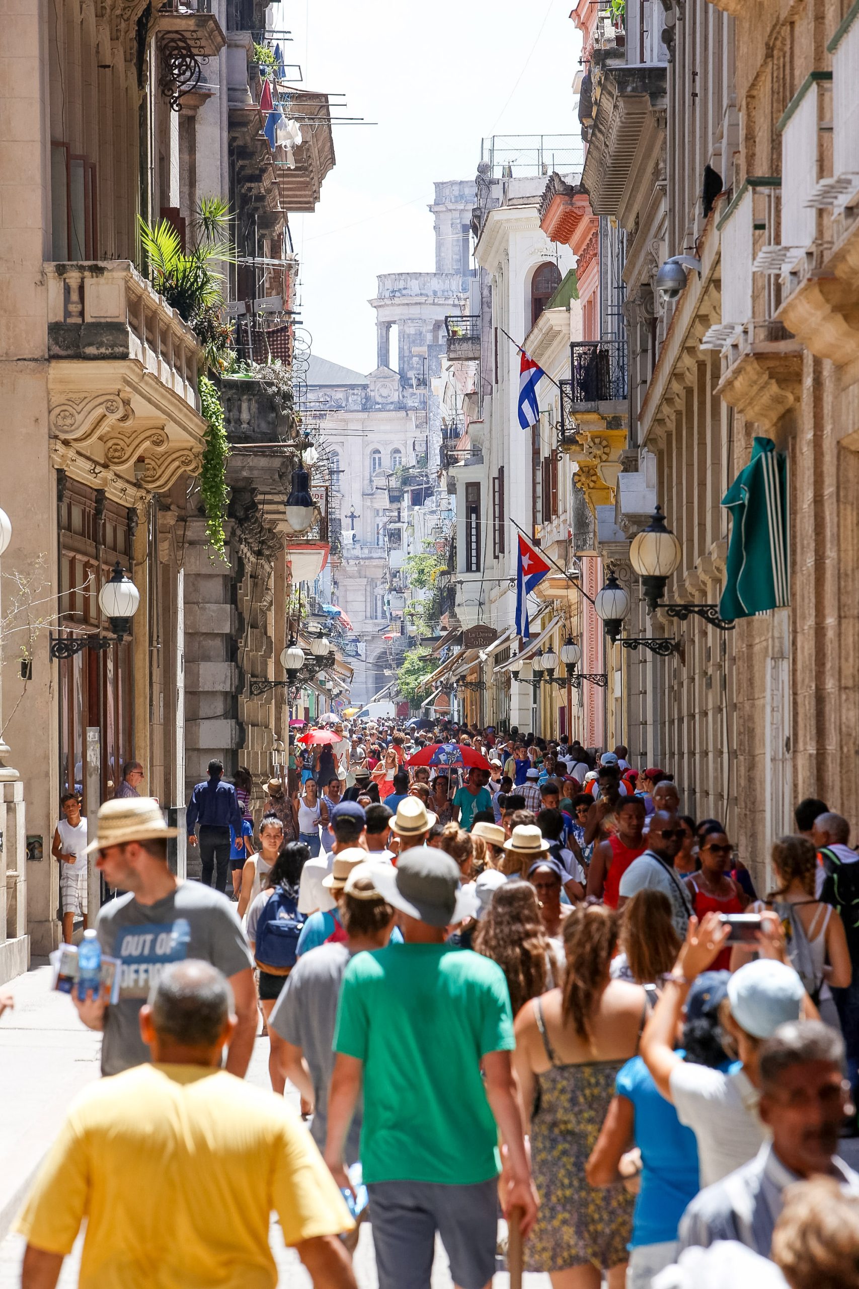 A crowded street in Old Havana with people walking past colonial buildings.