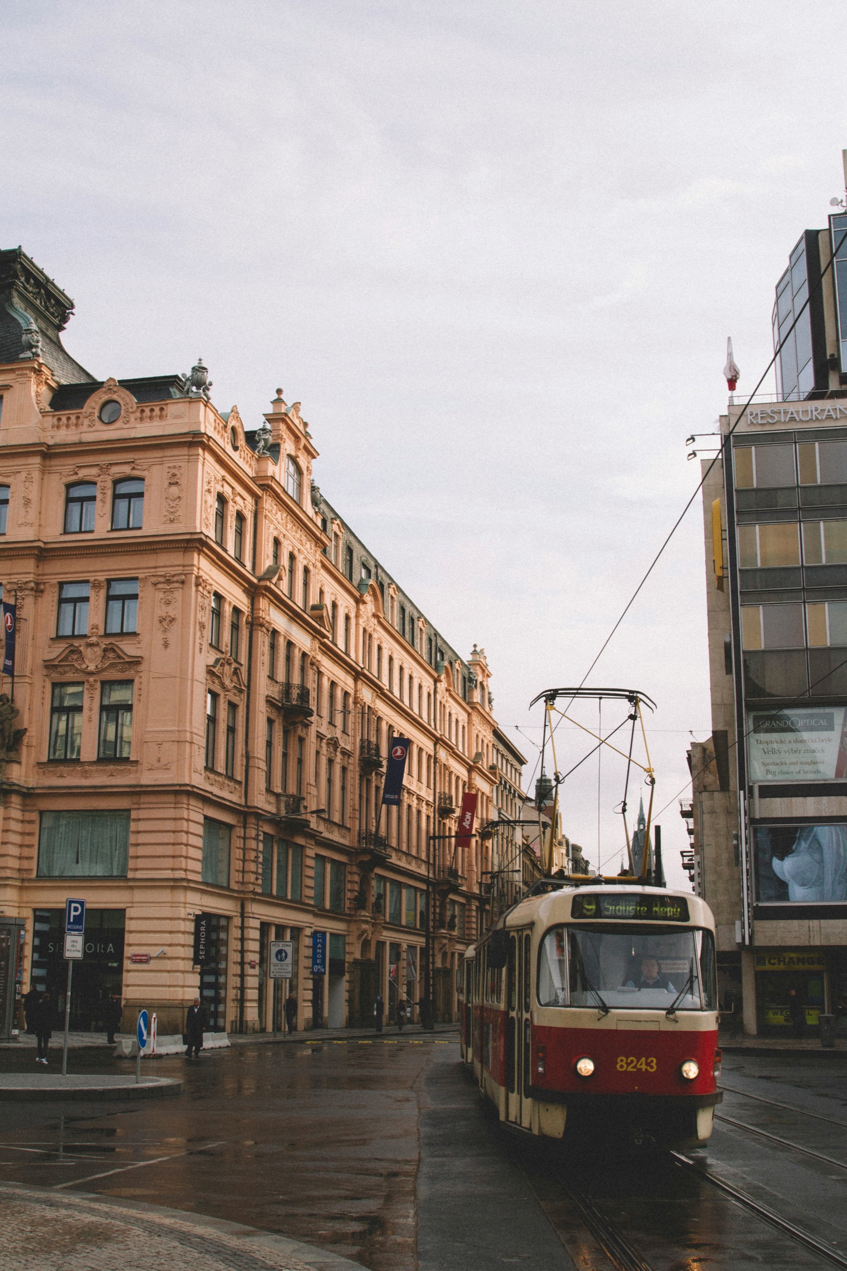 A red and cream tram turns past an ornate Art Nouveau facade on a wet city street.