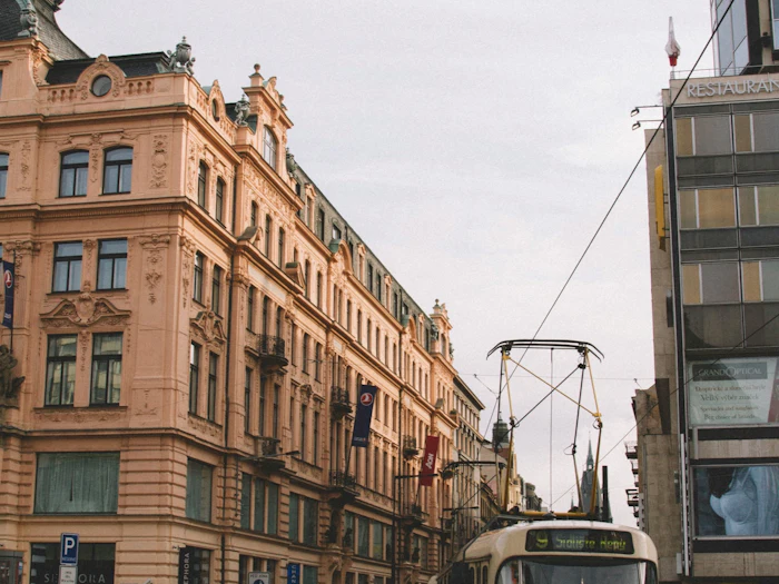 A red and cream tram turns past an ornate Art Nouveau facade on a wet city street.