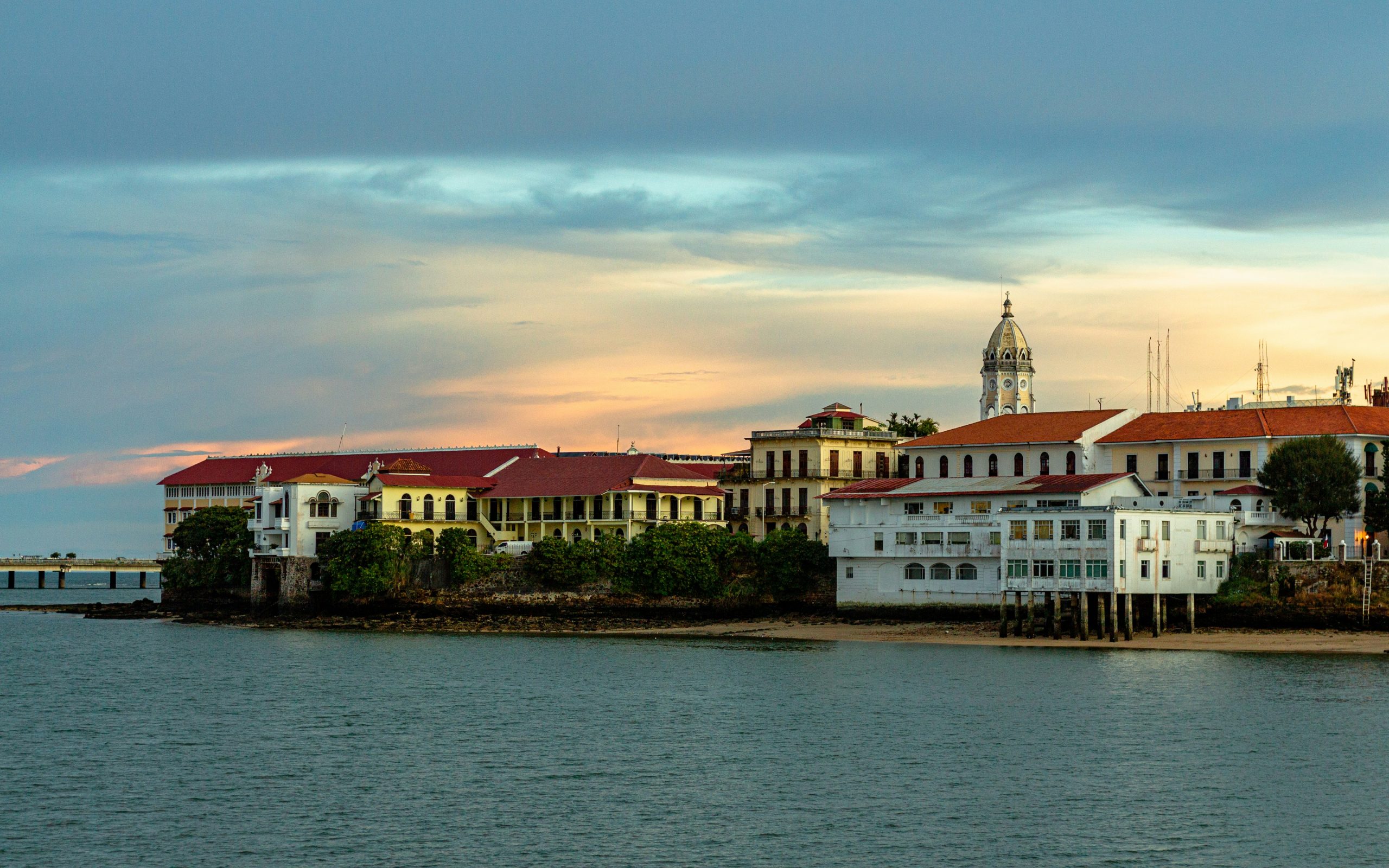 Colonial buildings and a church bell tower along the Casco Viejo waterfront at sunset.