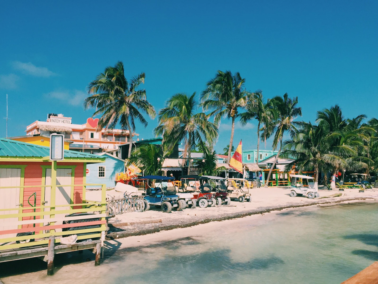 Colorful beachfront buildings and palm trees along the sand on Caye Caulker