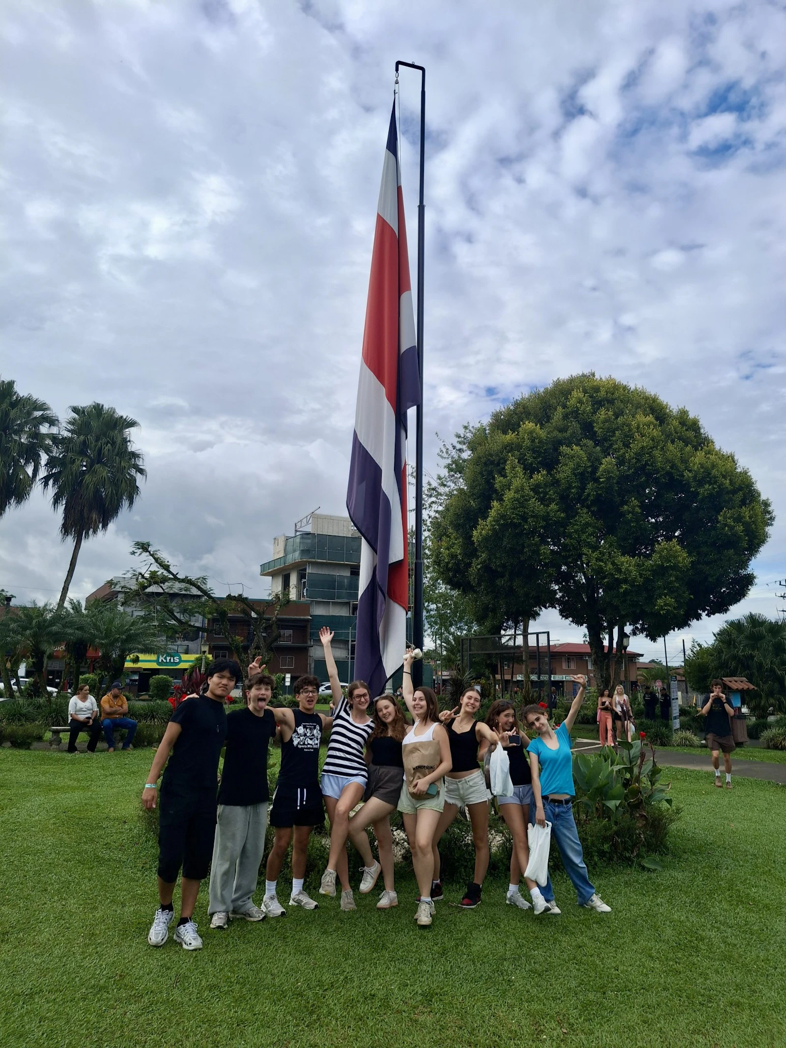 Students cheer beneath the Costa Rican flag on a cloudy day in La Fortuna
