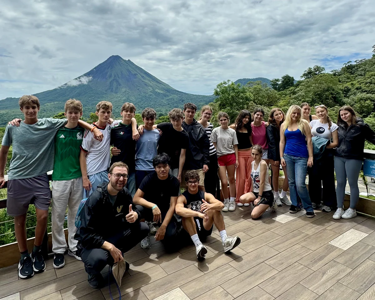 A Rustic Pathways student group stands on a deck in Costa Rica with Arenal Volcano rising behind them