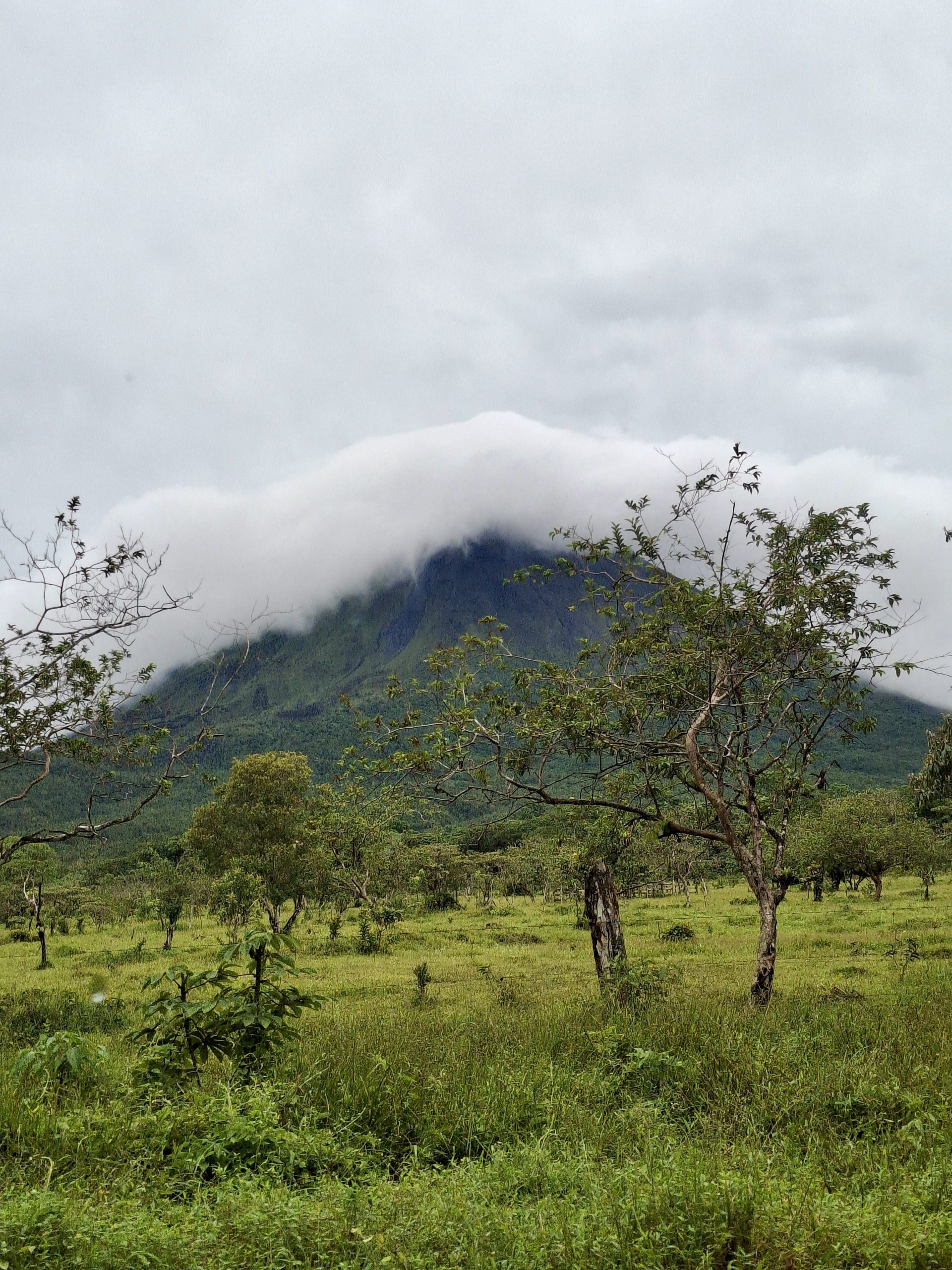 Clouds wrap the summit of Arenal Volcano above green farmland in Costa Rica