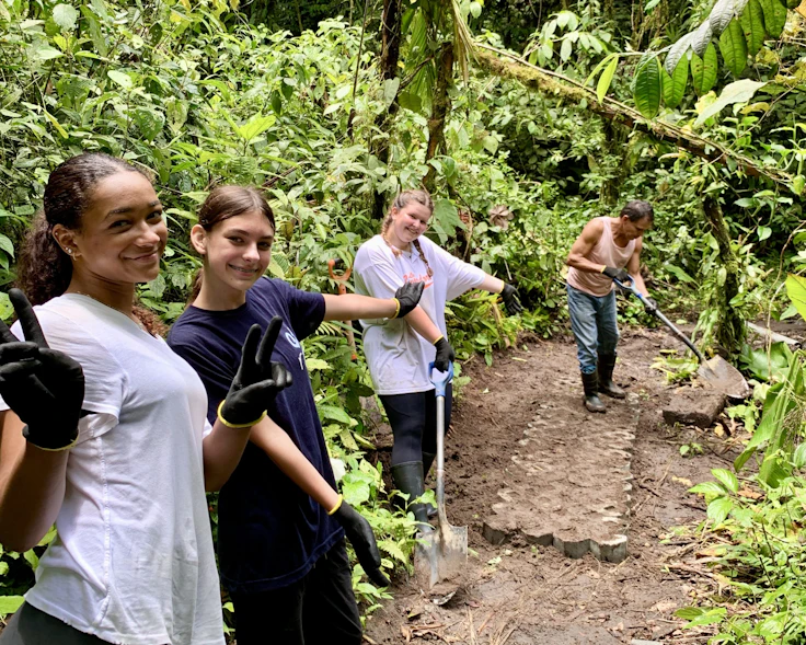 Smiling students in work gloves hold shovels on a forest trail service project in Costa Rica