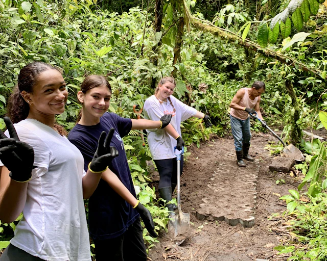 Smiling students in work gloves hold shovels on a forest trail service project in Costa Rica