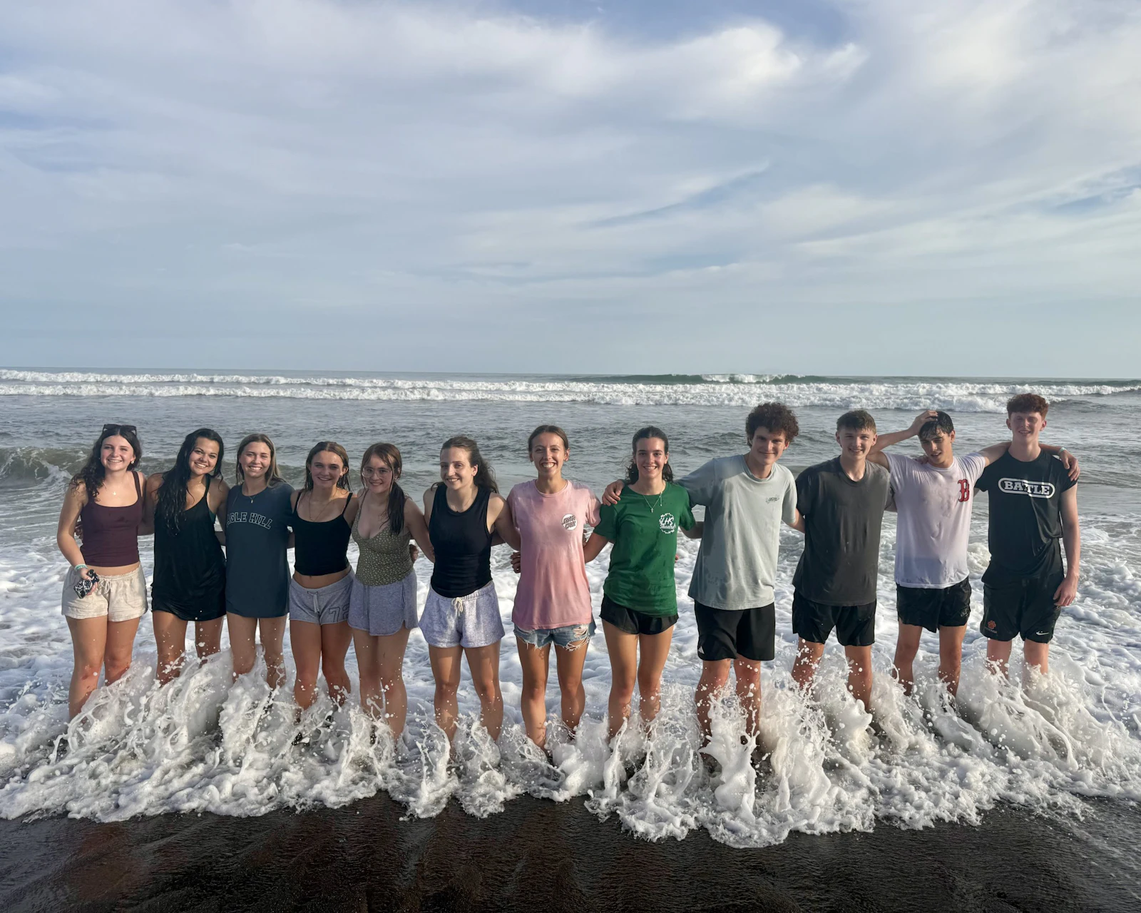 Students stand arm in arm in the shallow surf on a Costa Rica beach