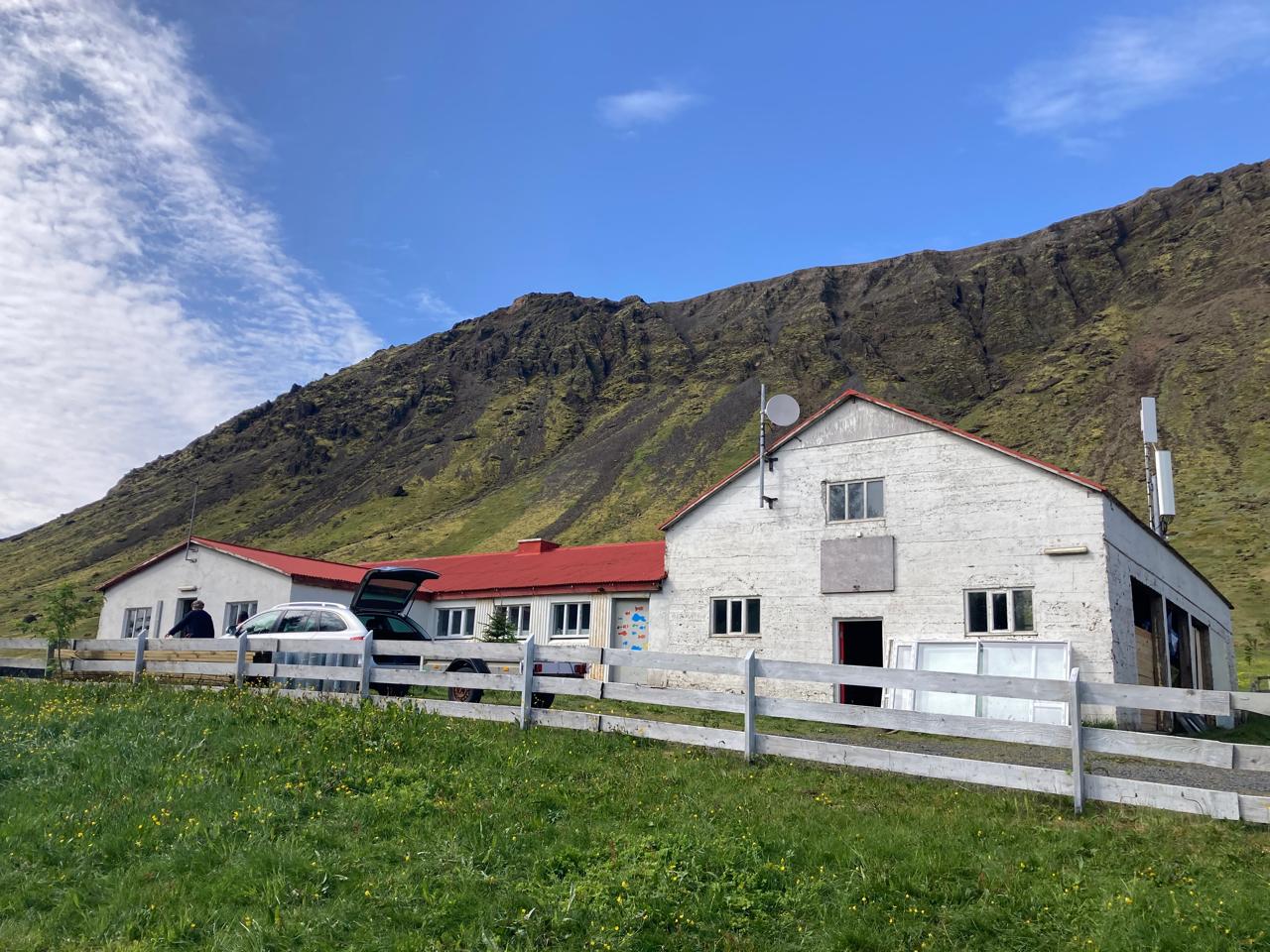 A red-roofed farmhouse sits below a steep mossy mountainside in Iceland