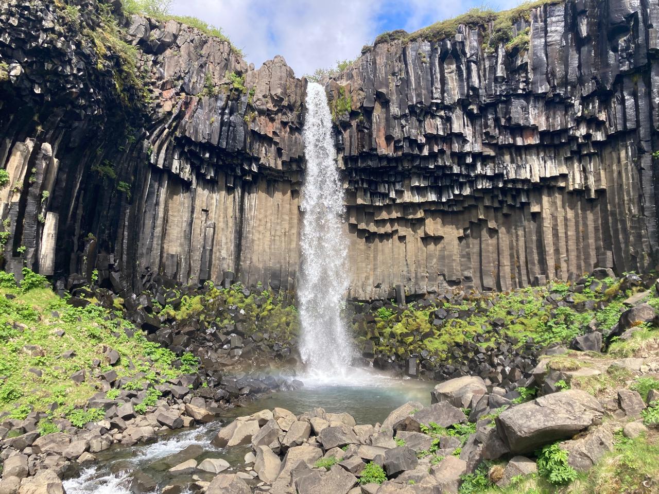 A waterfall drops through basalt columns into a rocky pool