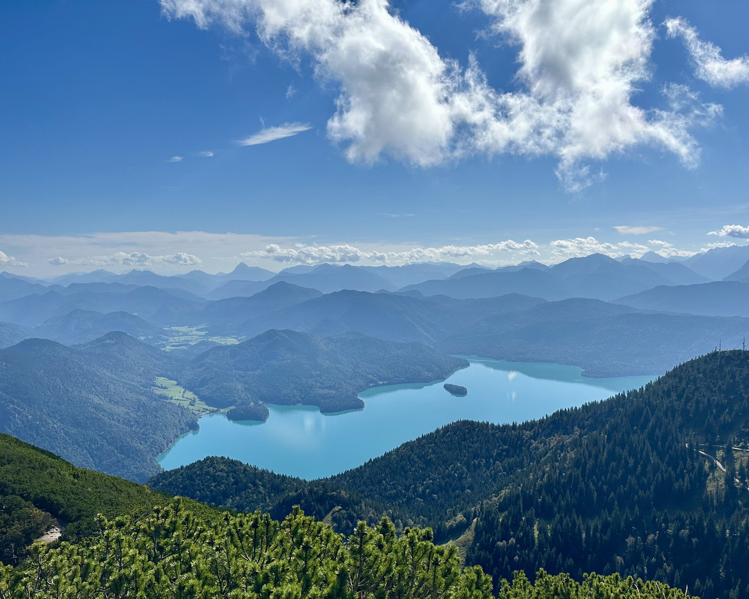 A turquoise lake winds between forested mountains, seen from high above