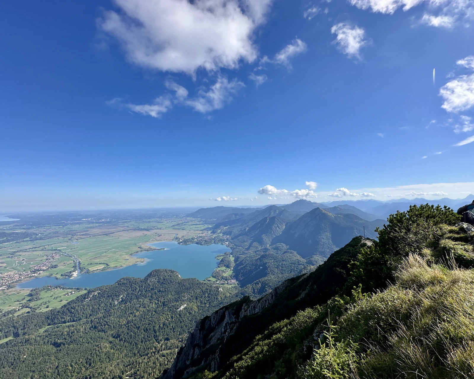 A lake and a wide green plain spread out below a grassy mountain summit