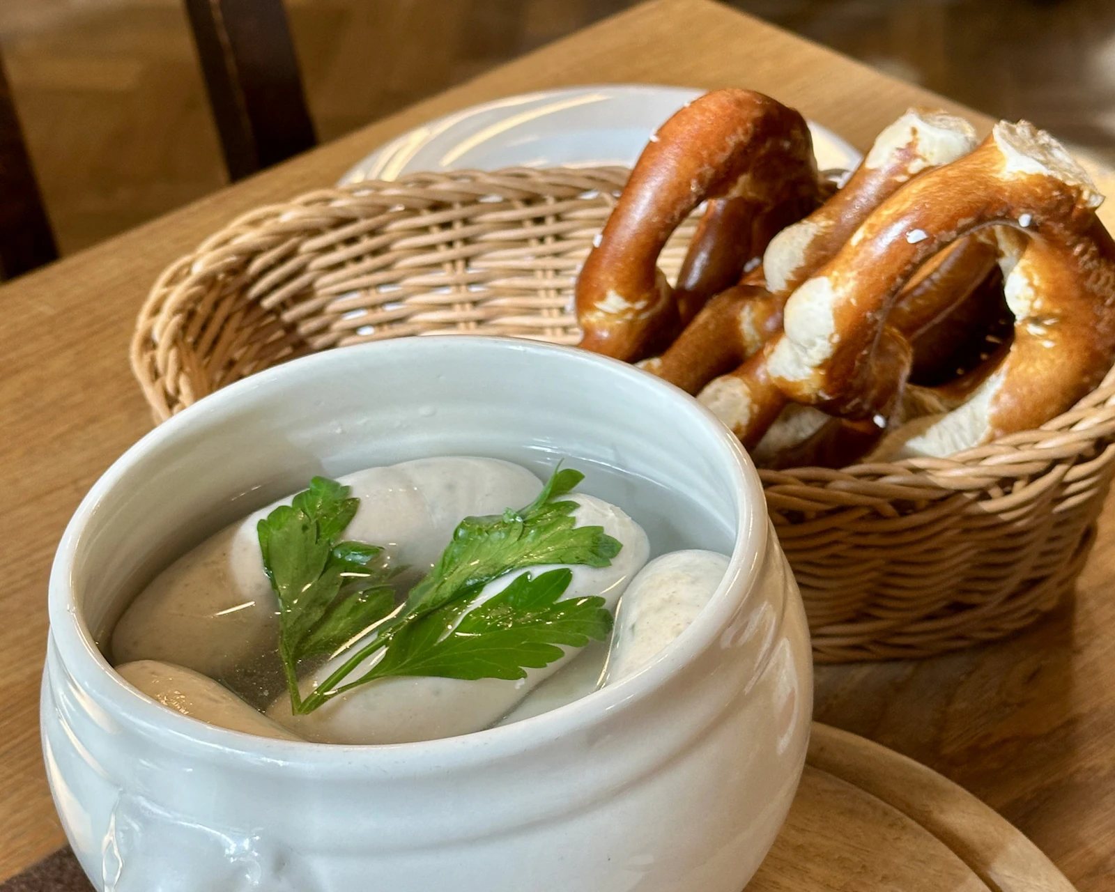 White sausages in a bowl of hot water beside a basket of pretzels