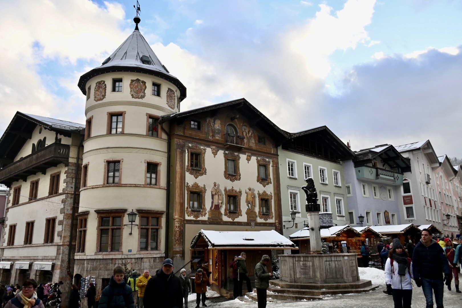 Painted facades and a clock tower line a snowy town square with market stalls