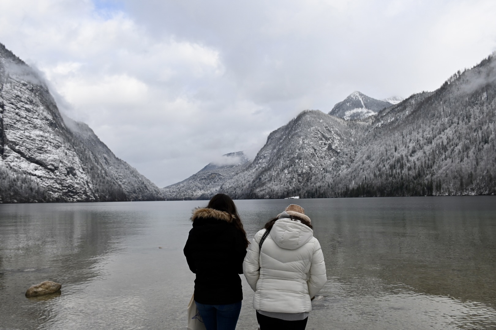 Two teen travelers enjoy a peaceful winter view of Lake Königssee, surrounded by snow-dusted mountains during a student travel adventure in Germany.