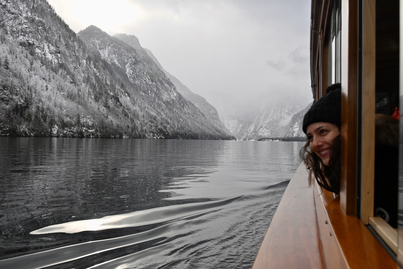 Student travelers lean out a boat window to view snowy alpine peaks along a lake
