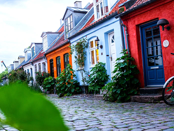 Pastel-painted cottages with climbing roses along the cobbled lane of Møllestien in Aarhus, a bicycle parked by a blue door.