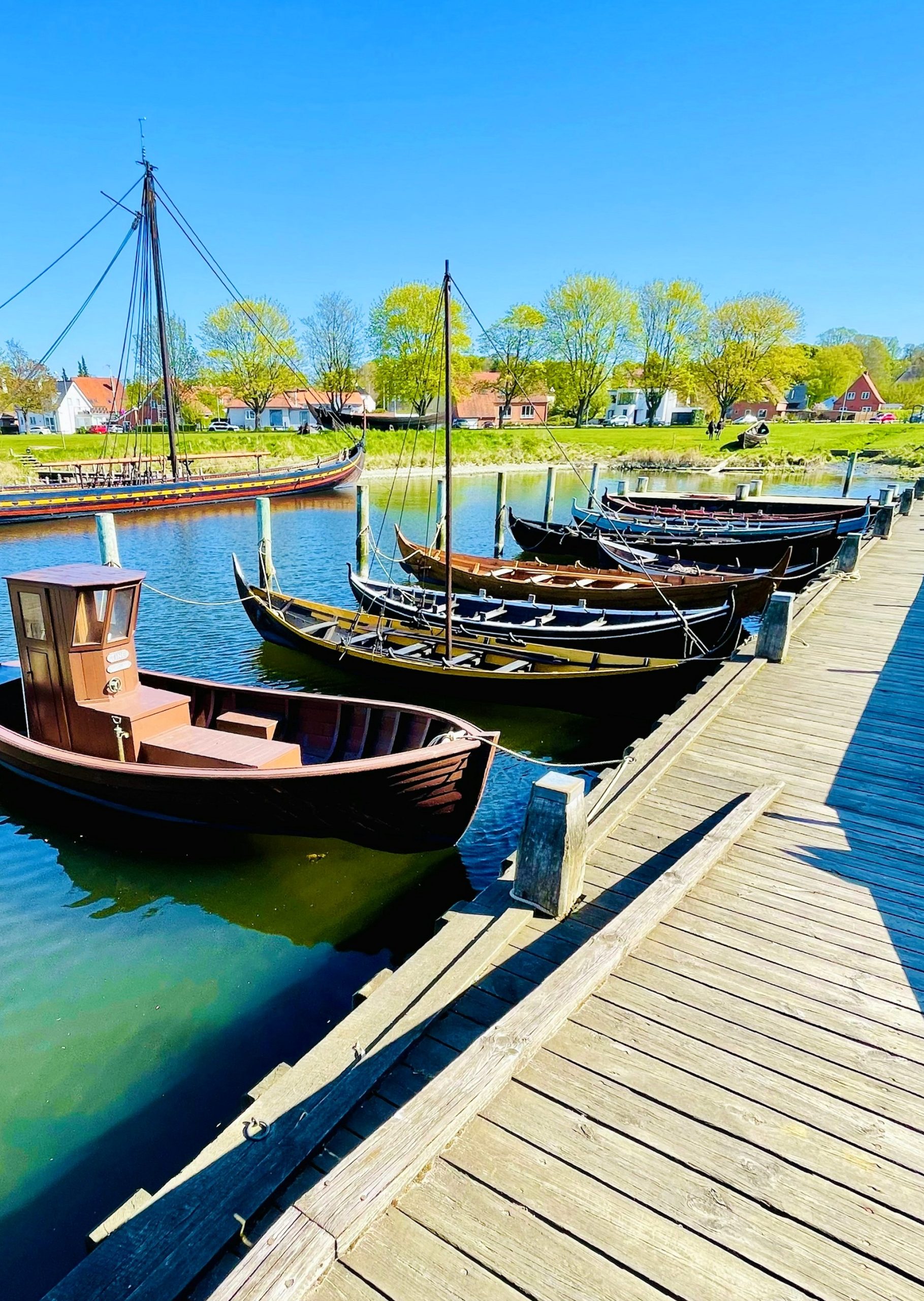 Reconstructed wooden Viking-style boats moored along a timber jetty in the museum harbor at Roskilde under a clear sky.