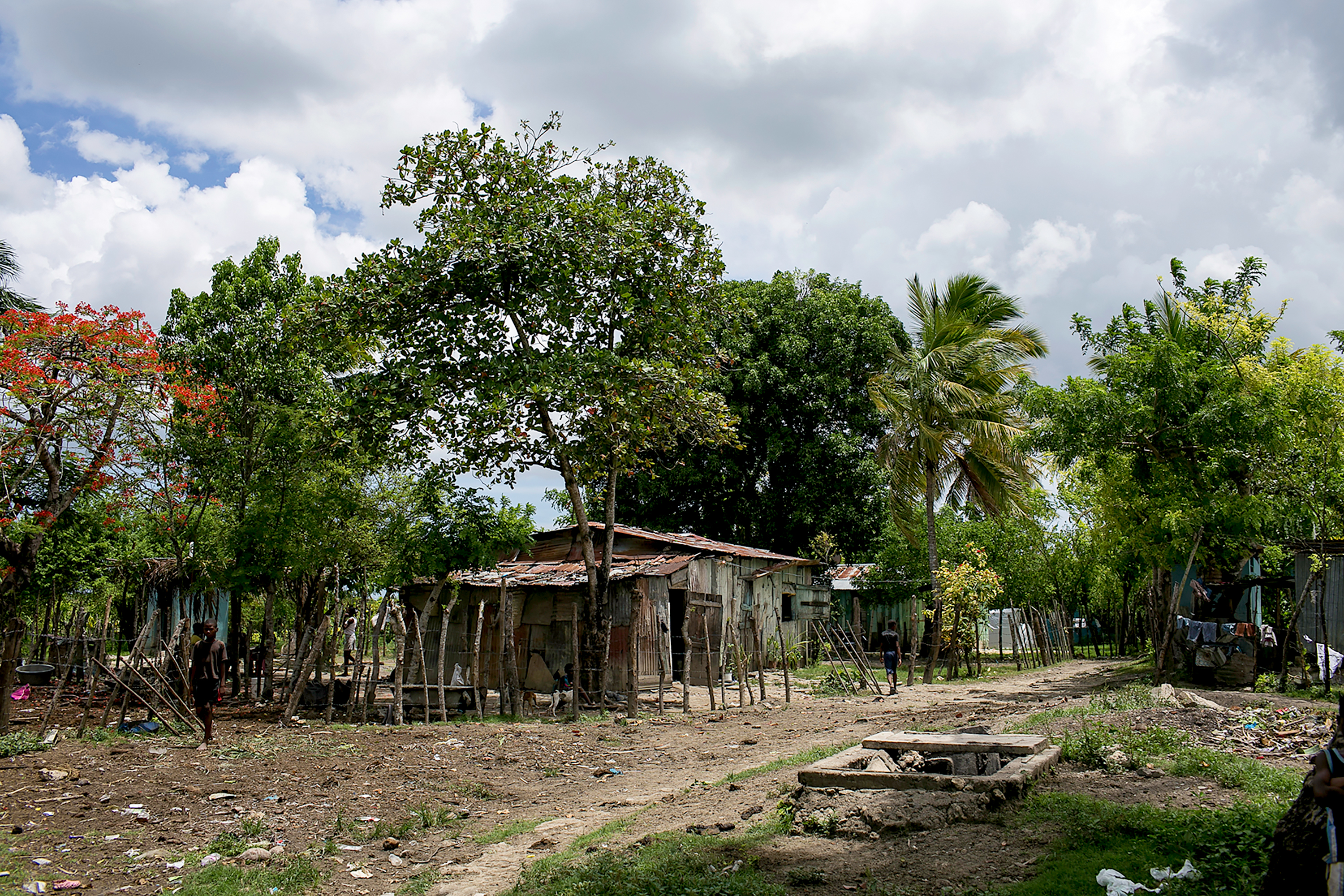 A modest home with a tin roof sits among trees in a batey community