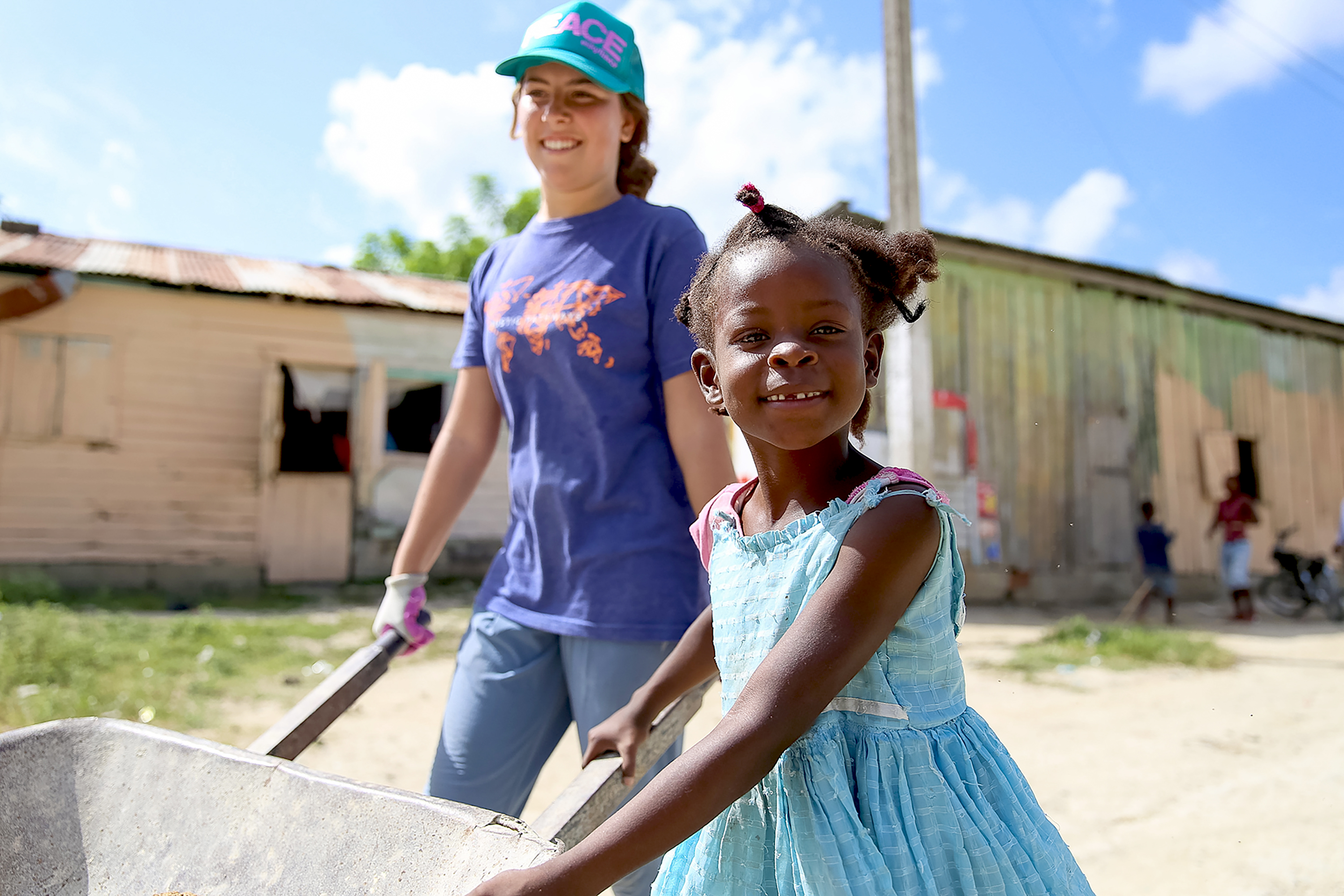 A student and a local child push a wheelbarrow together in a batey community
