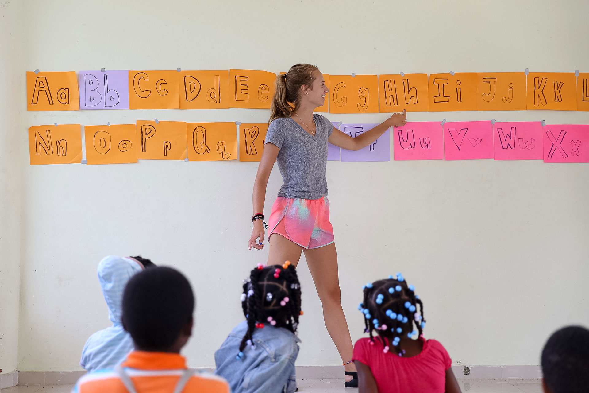 On this school trip, a student points to alphabet flashcards on the wall while young children watch from below