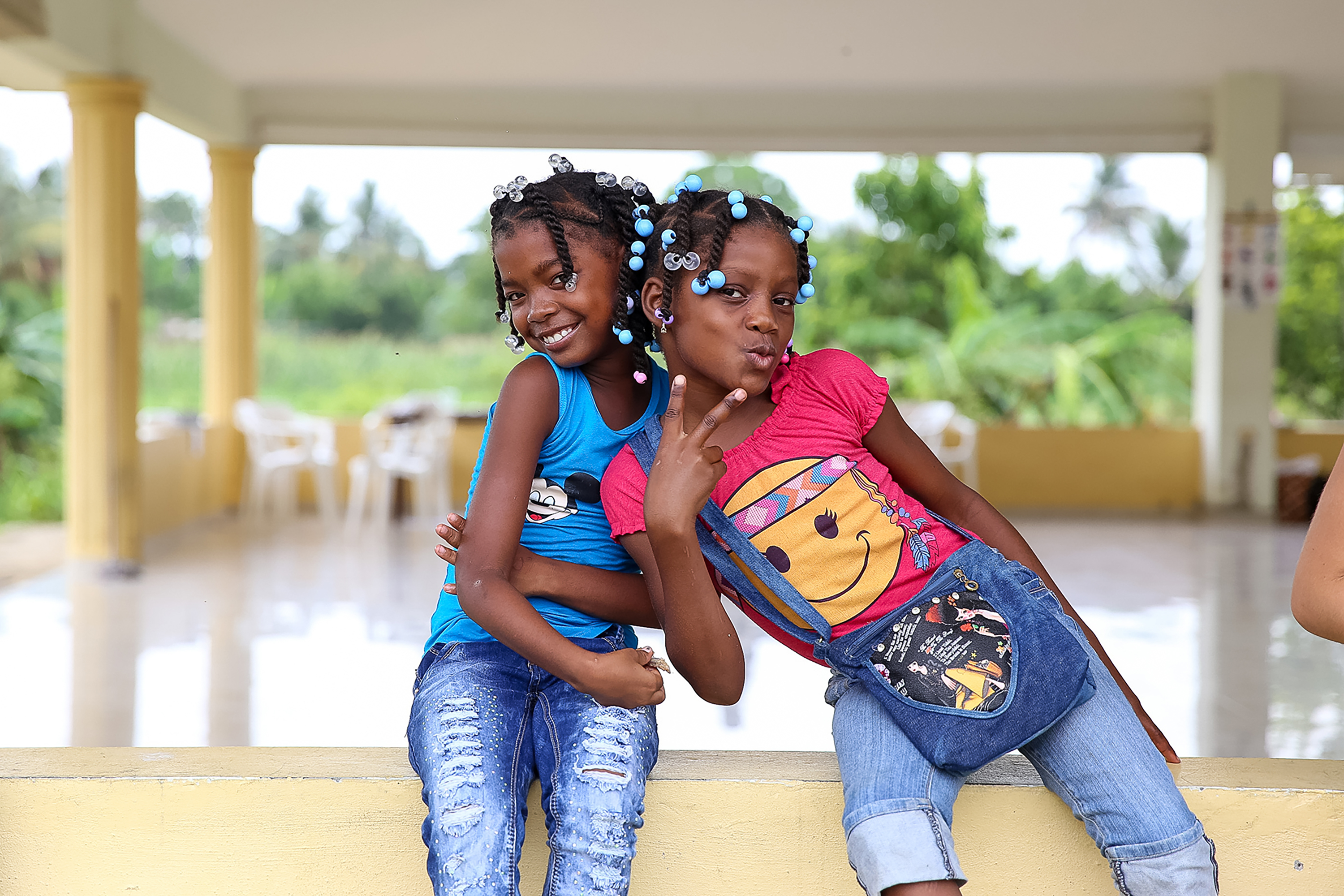 Local girls with beaded braids pose together on a porch ledge
