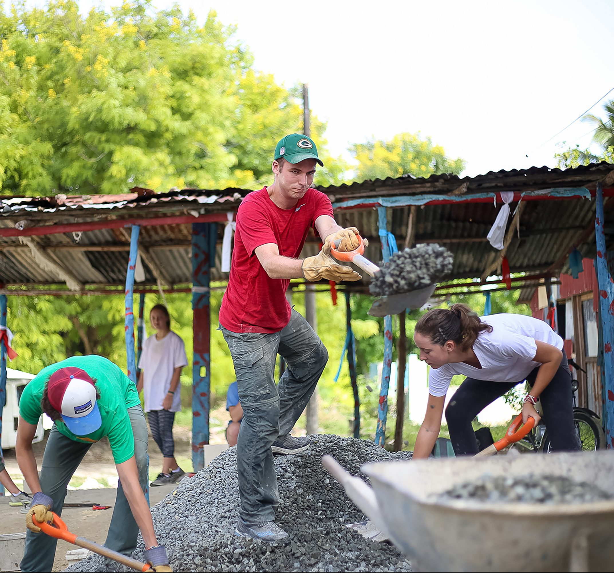Teens shovel and mix gravel for a concrete service project in a village