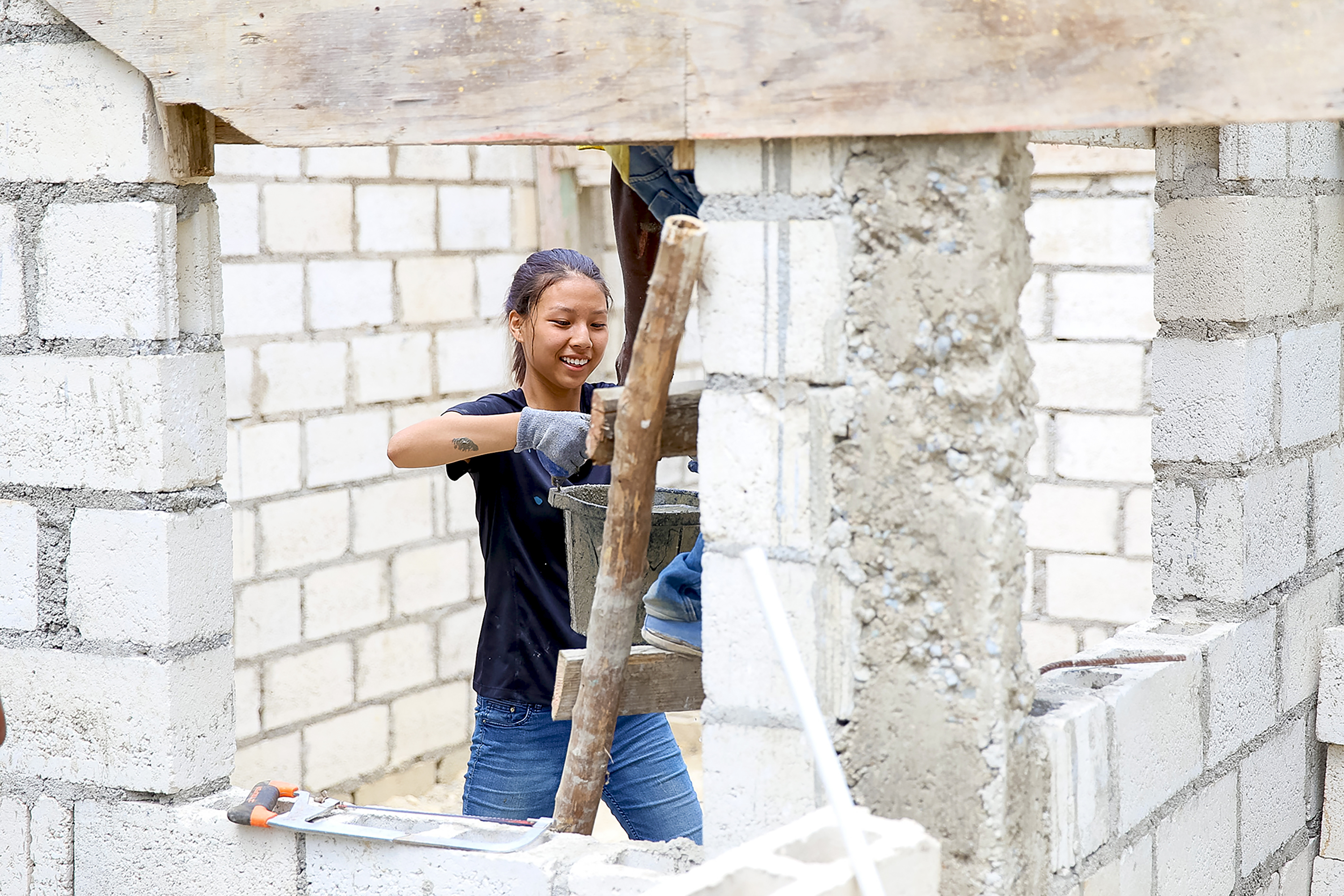 A student smiles while mixing cement at a cinder block construction site