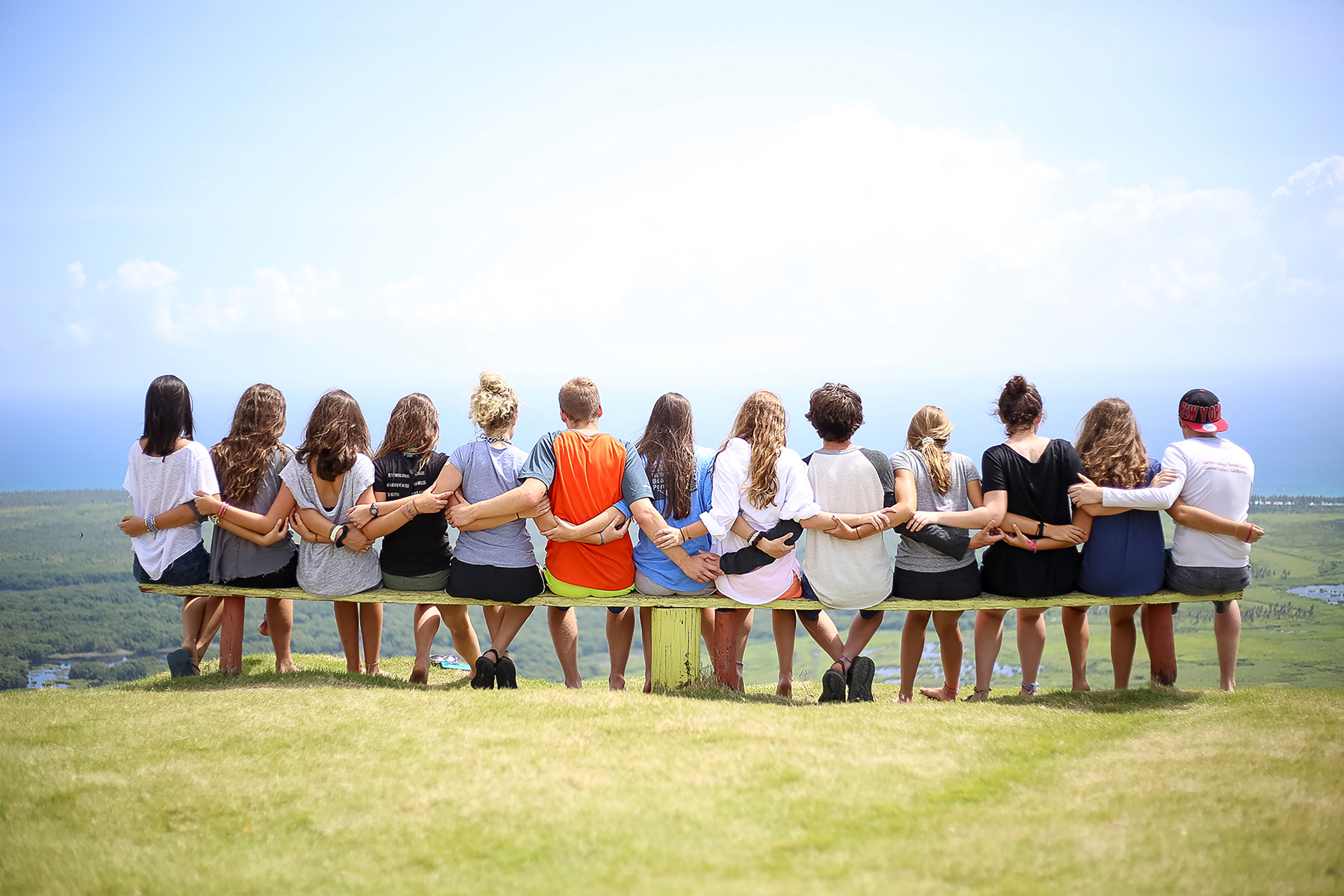 Students sit arm-in-arm on a bench overlooking green fields and the coast