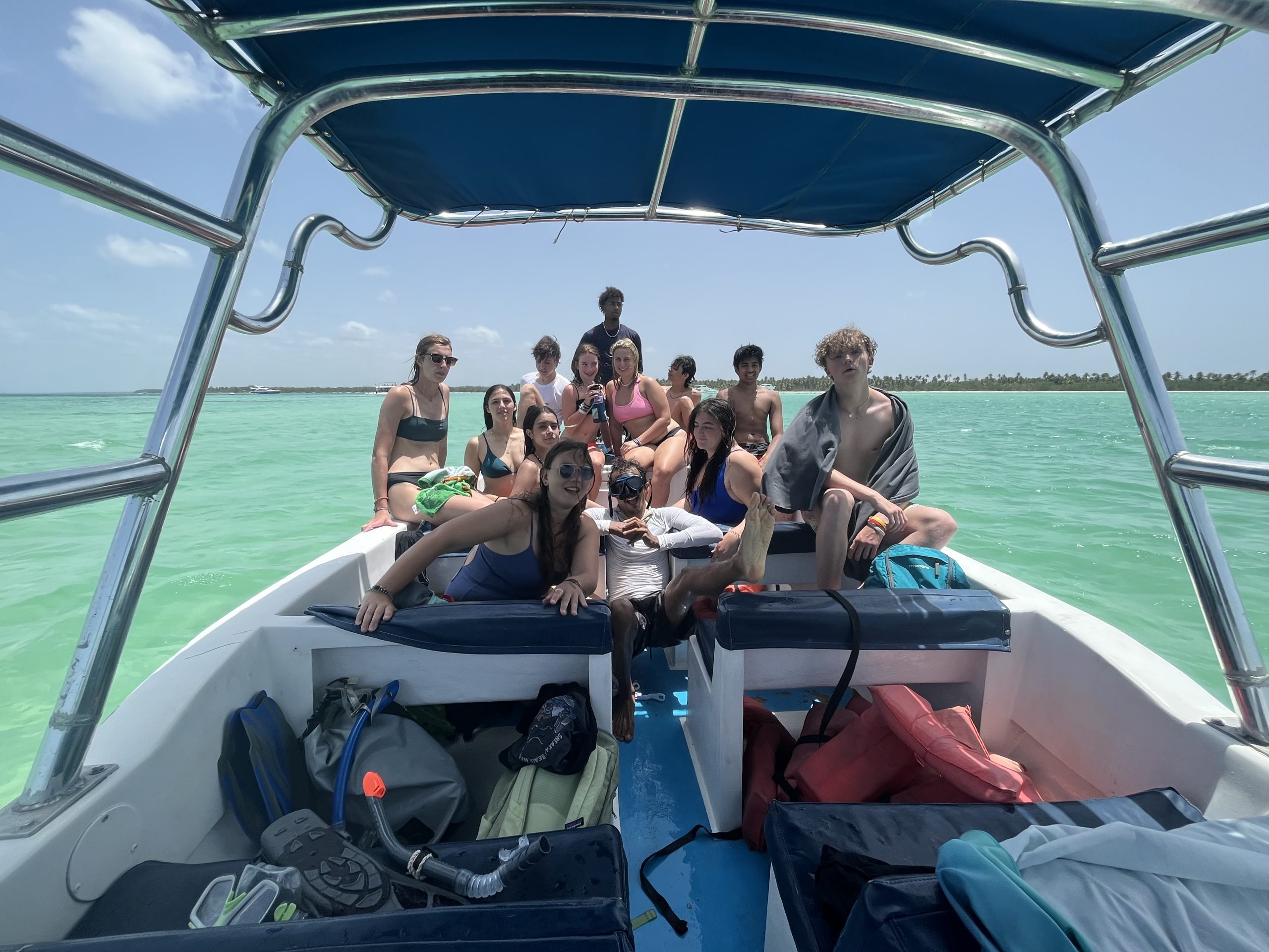 Students relax on the bow of a boat over turquoise water with snorkel gear stowed nearby