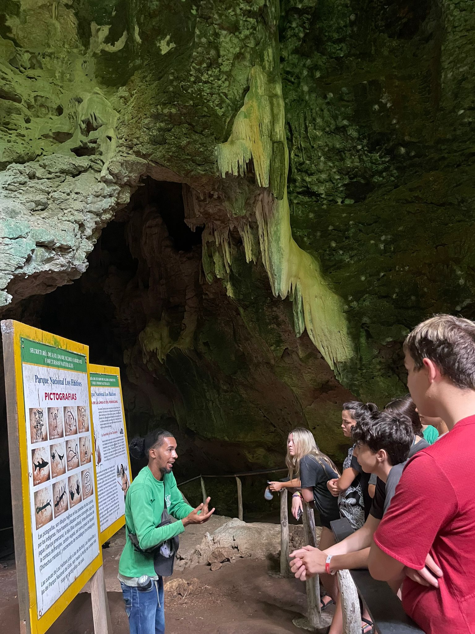 A guide describes cave formations to students beside an informational sign underground