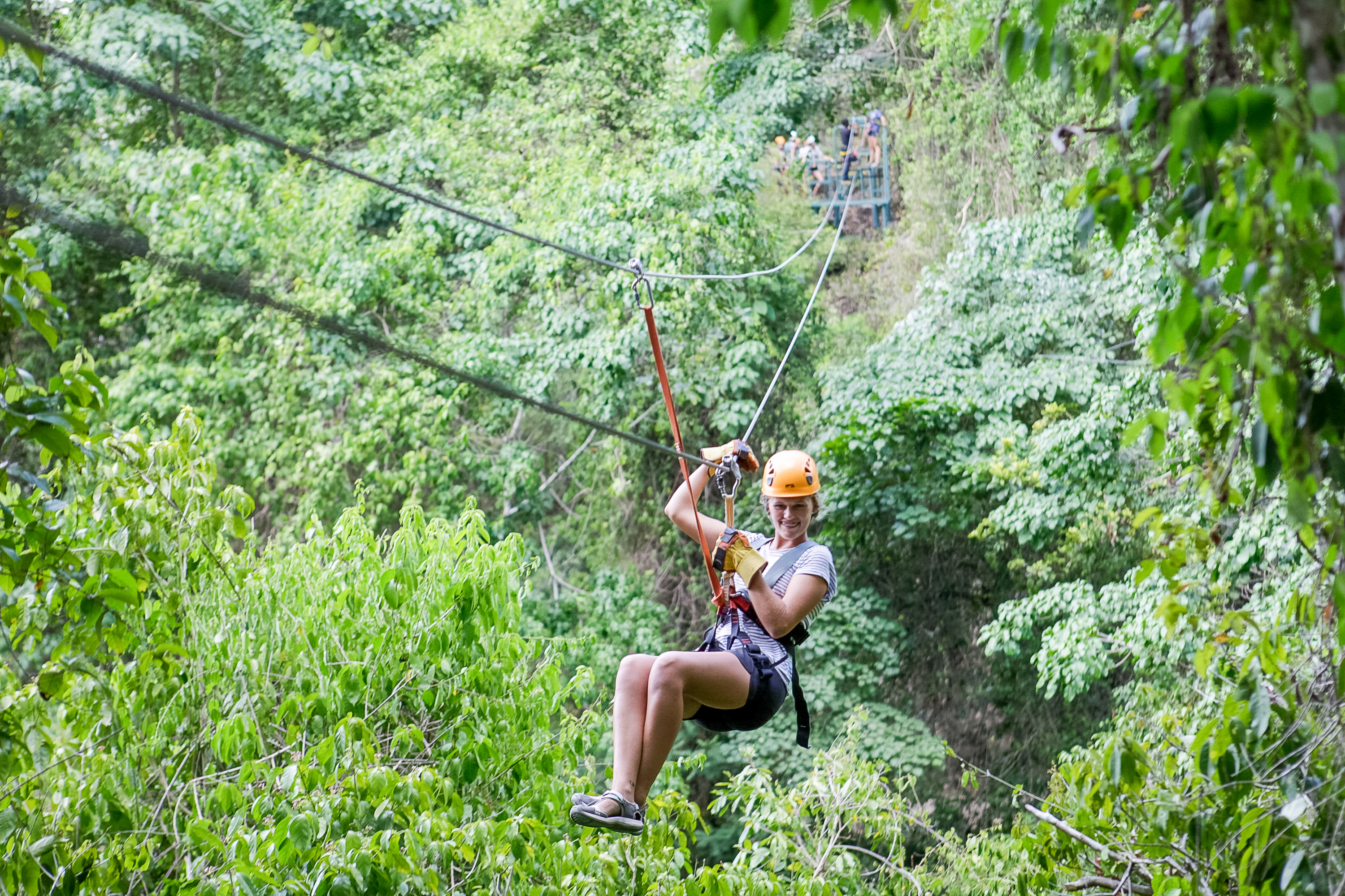 Teens zipline through a lush green forest canopy