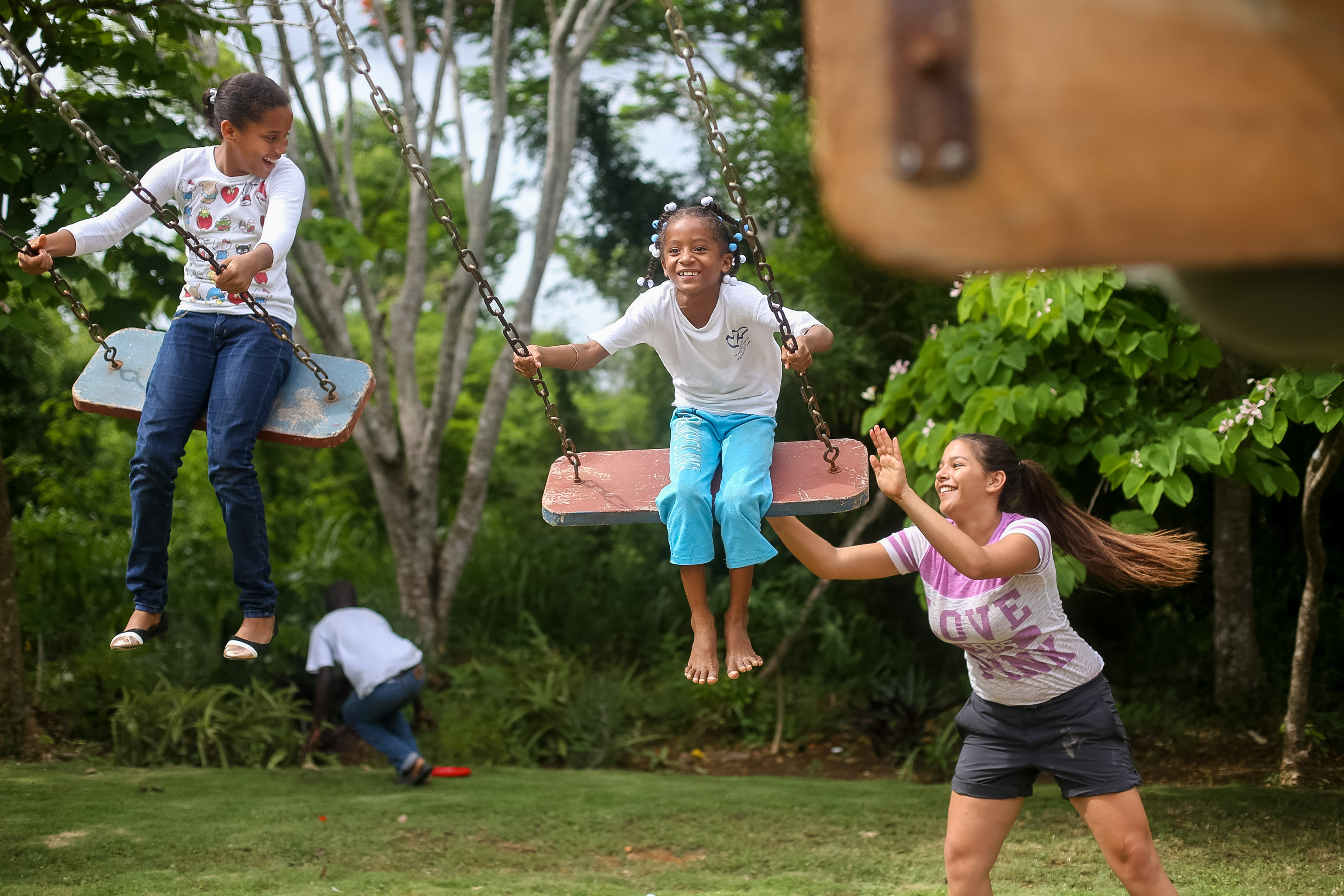 Children swing on wooden swings while a student pushes one from behind
