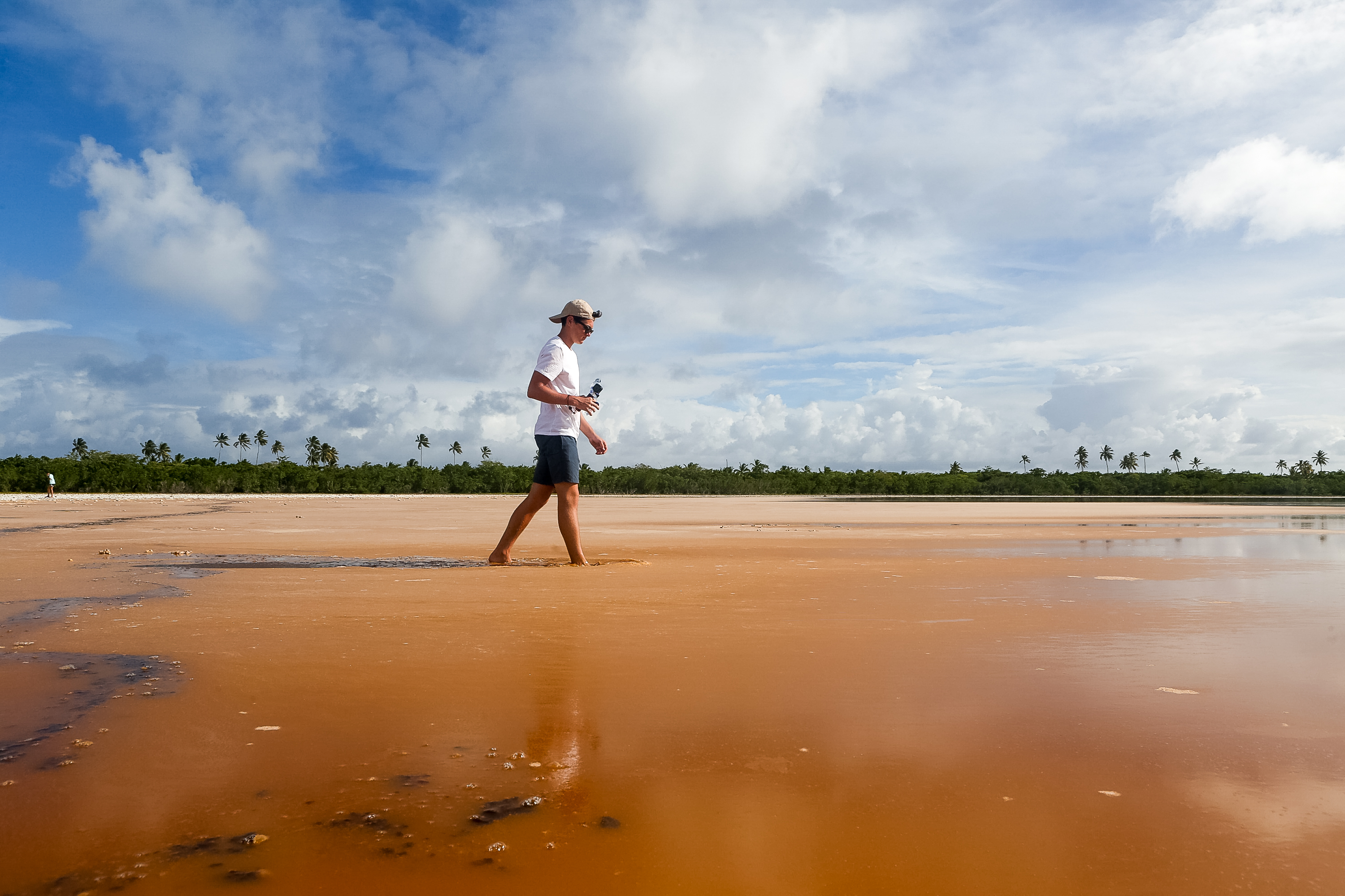 A student walks across a wide tidal flat with palm trees along the horizon