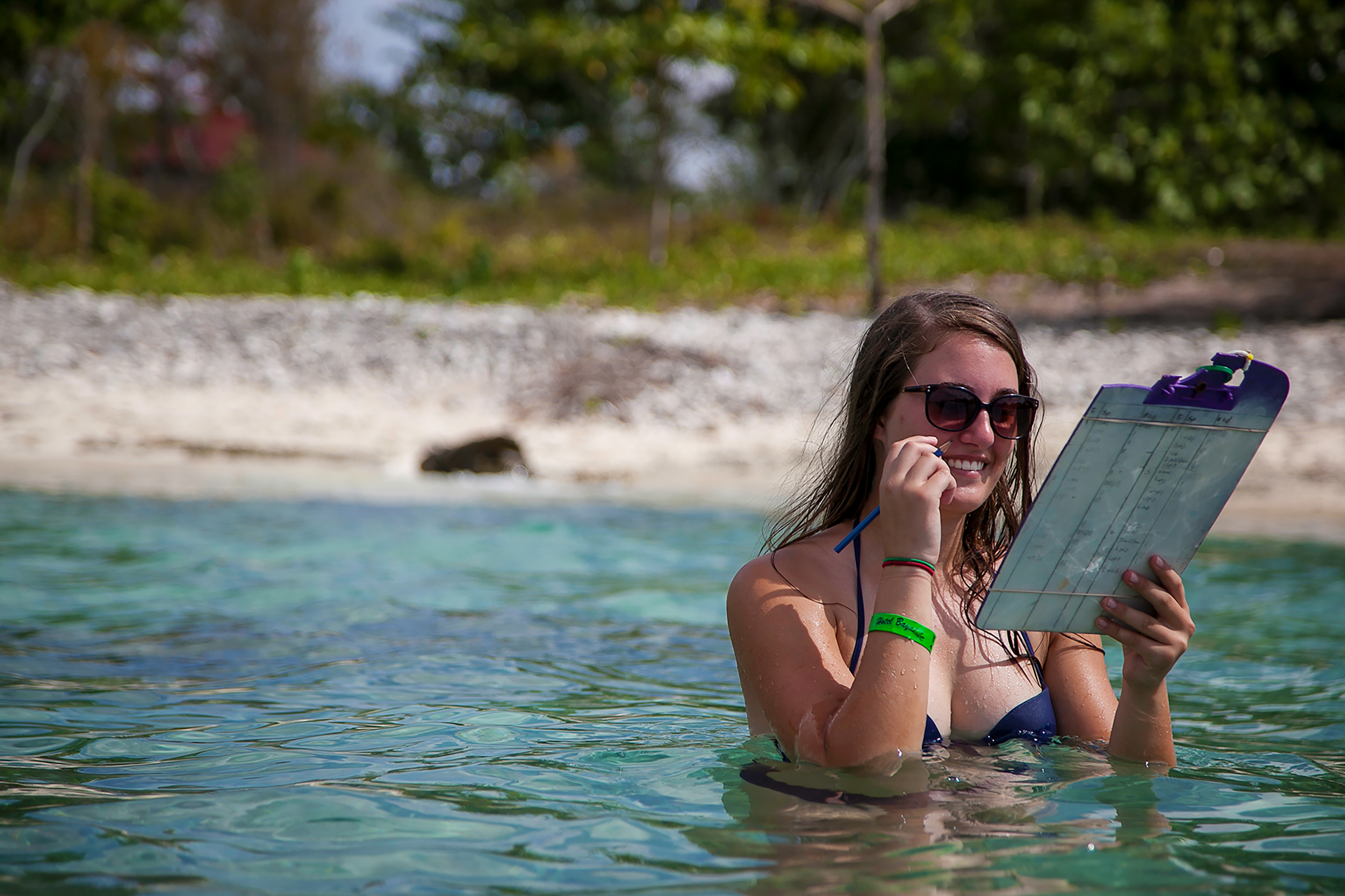 A student reviews data on a clipboard while wading in shallow coastal water