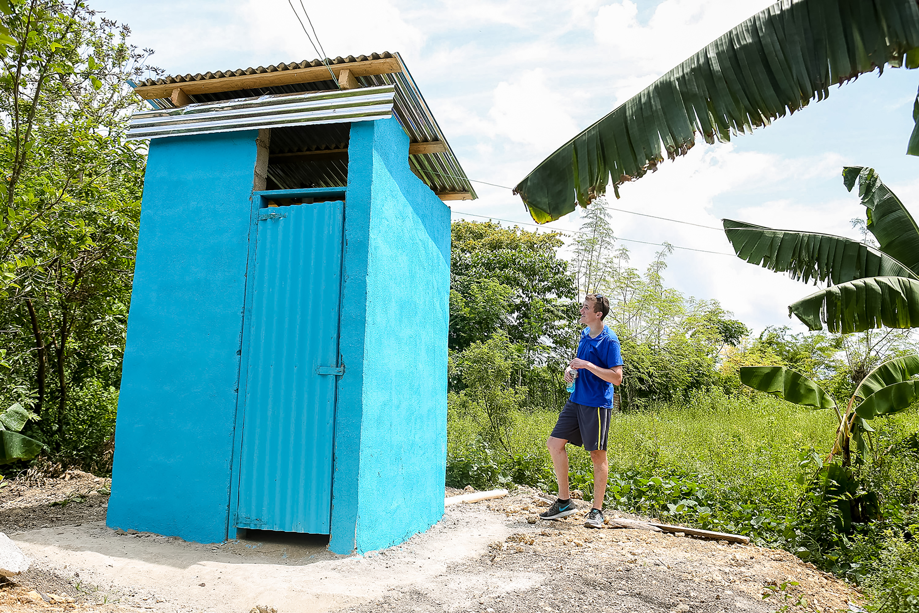 Student travelers stand beside a newly built blue latrine structure