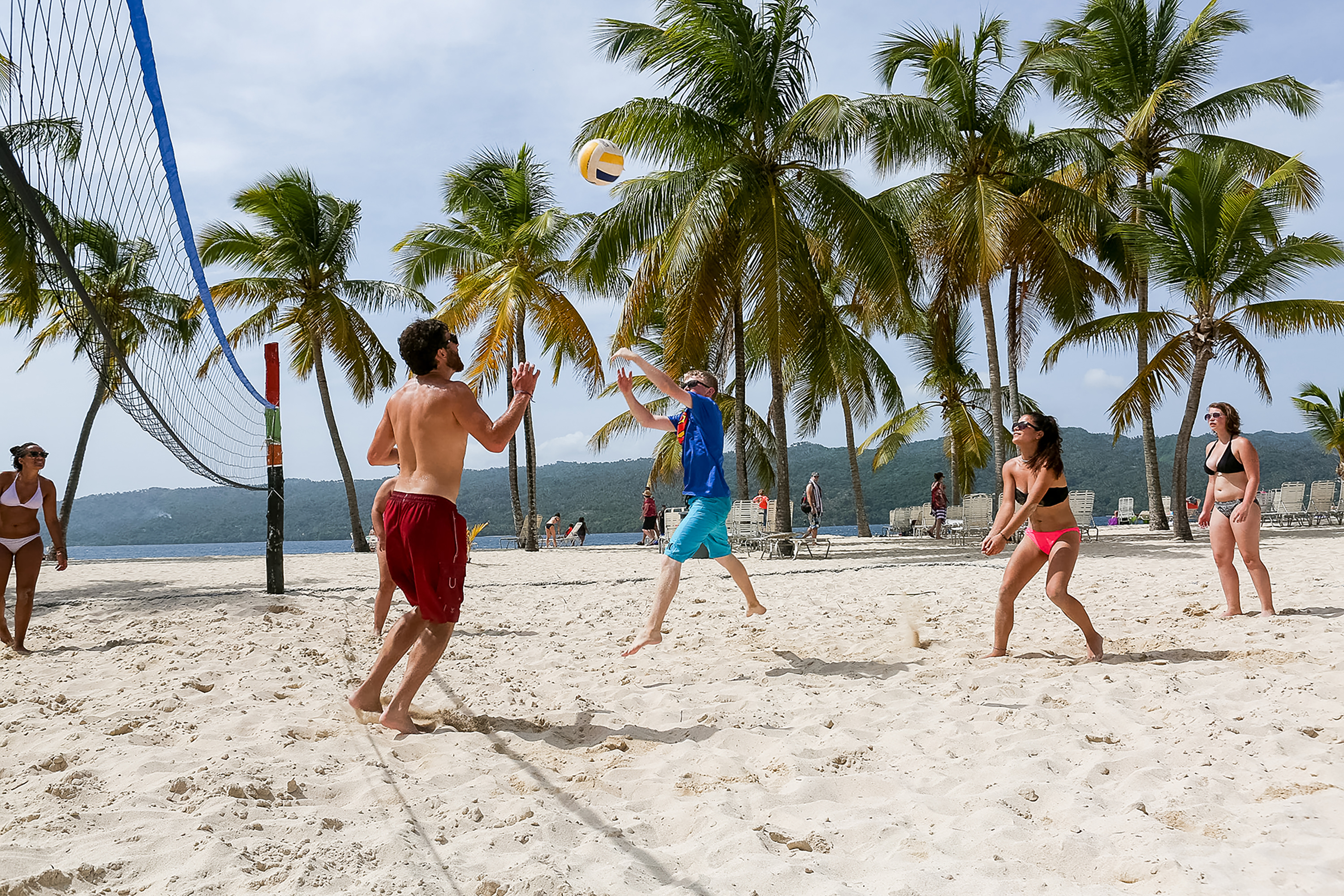 Teens play beach volleyball under palm trees