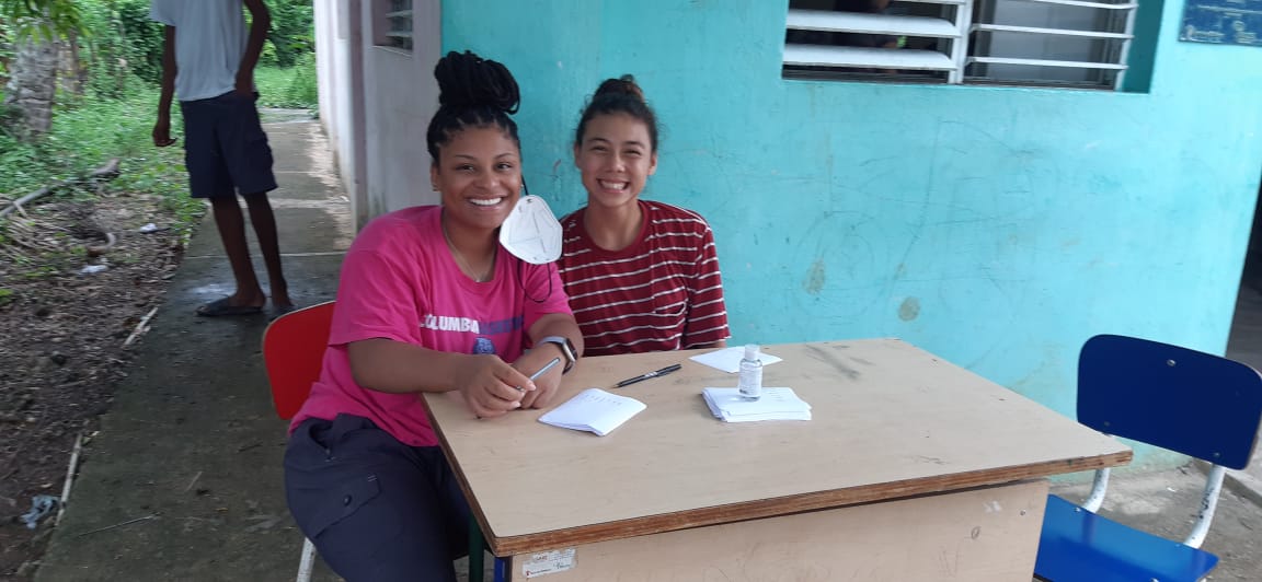 Students sit at a table outside a teal building during a community health workshop