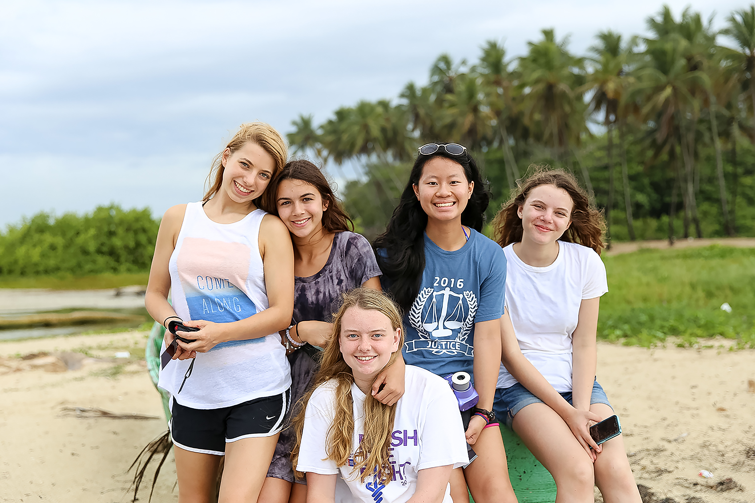 Students smile together on a palm-lined beach