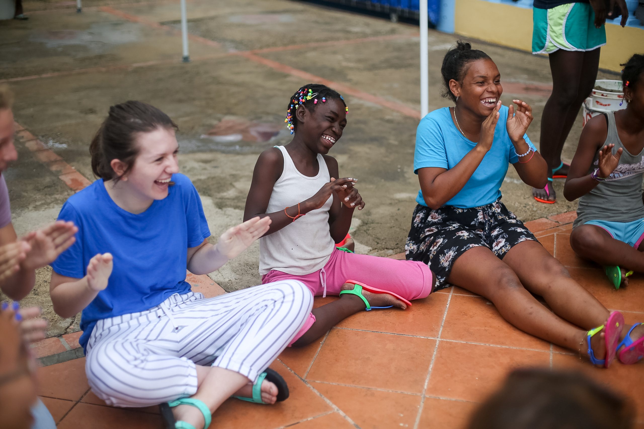 Students sit on a tiled patio, laughing and clapping together