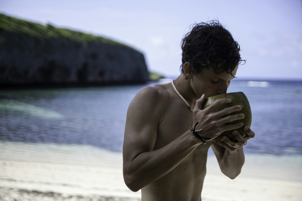 Student drinking from a coconut on a tropical beach during a short-term volunteer abroad trip focused on cultural immersion and service.