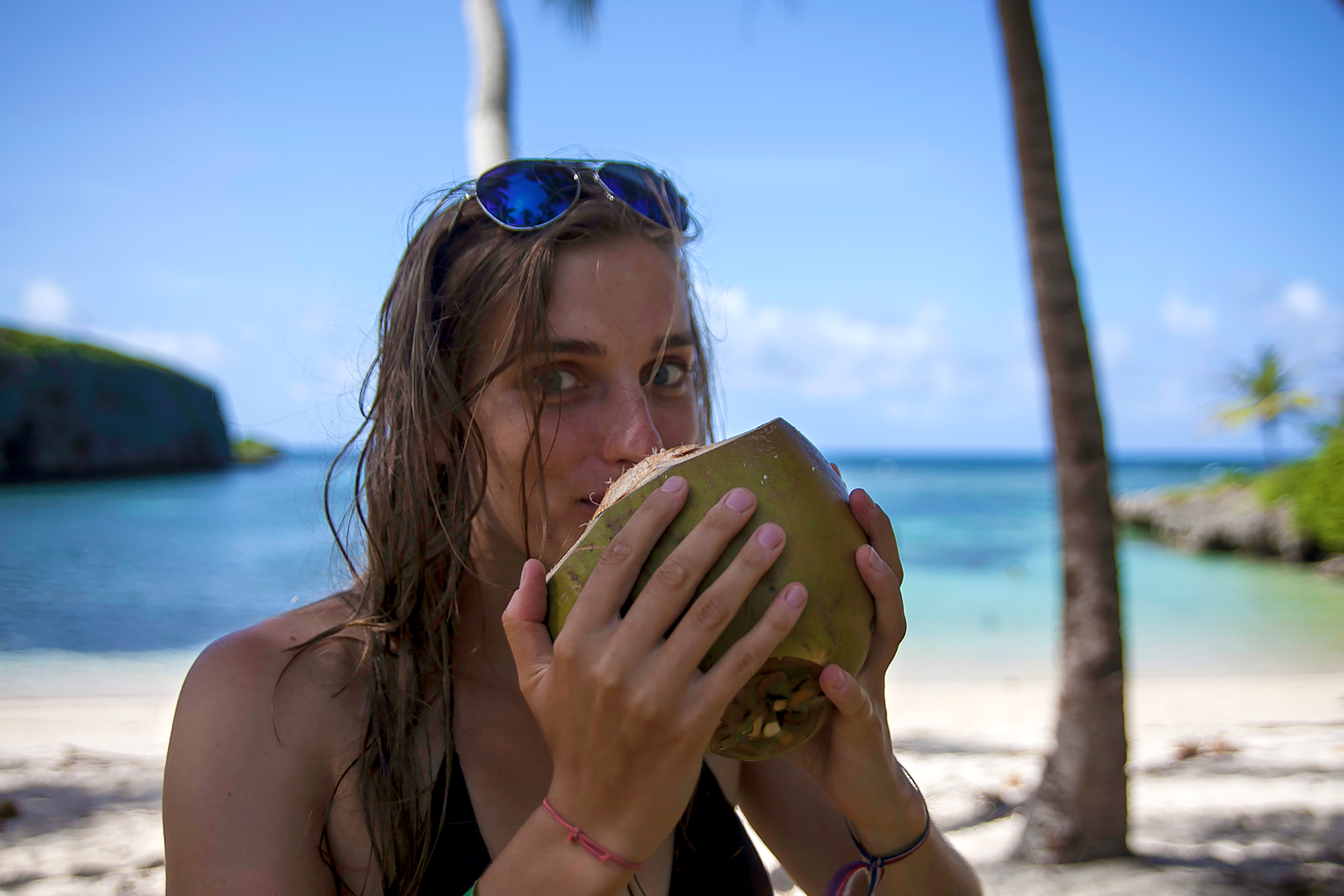 A student drinks from a fresh coconut on a palm-lined beach