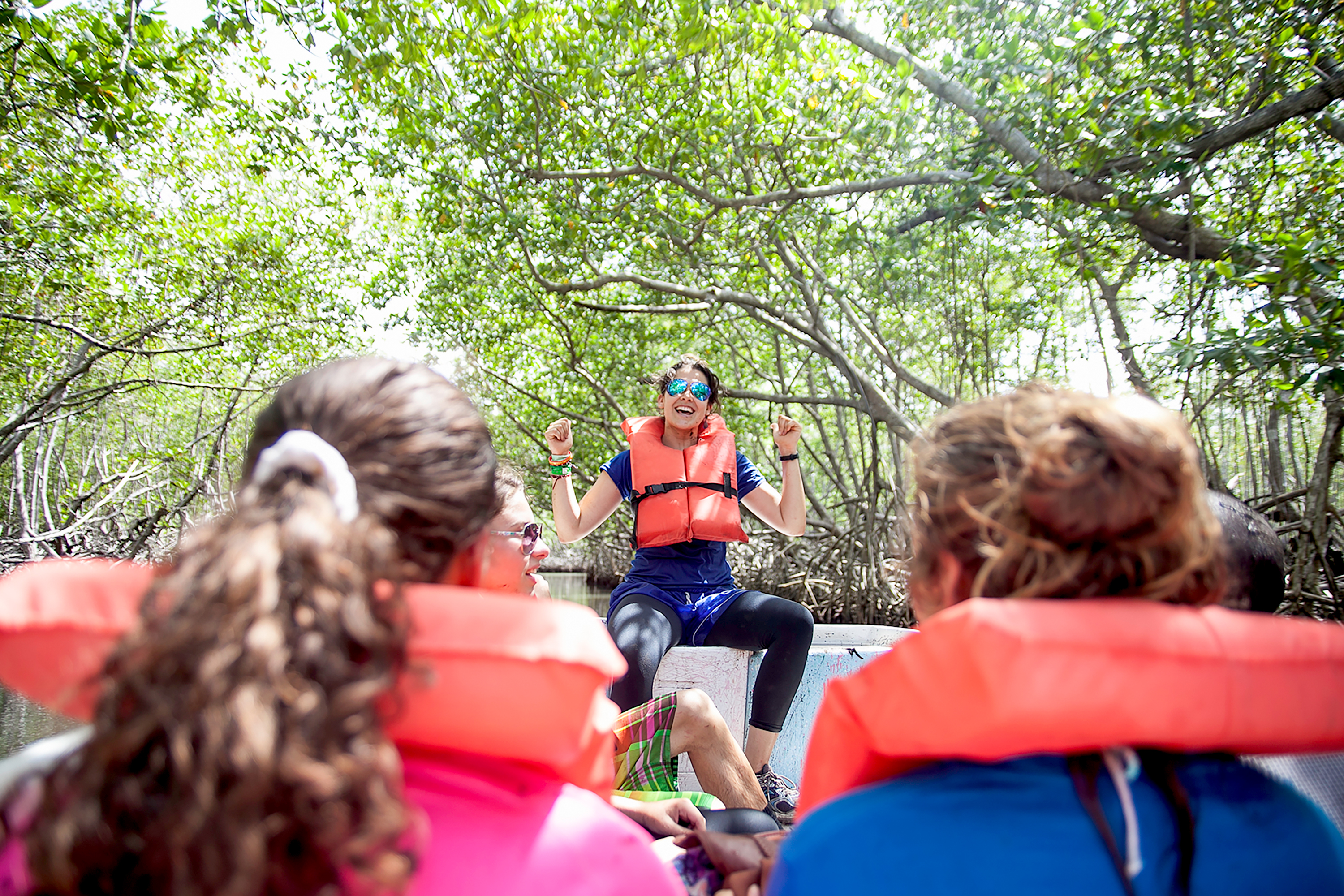 A guide in a life vest talks to students on a boat during a mangrove tour
